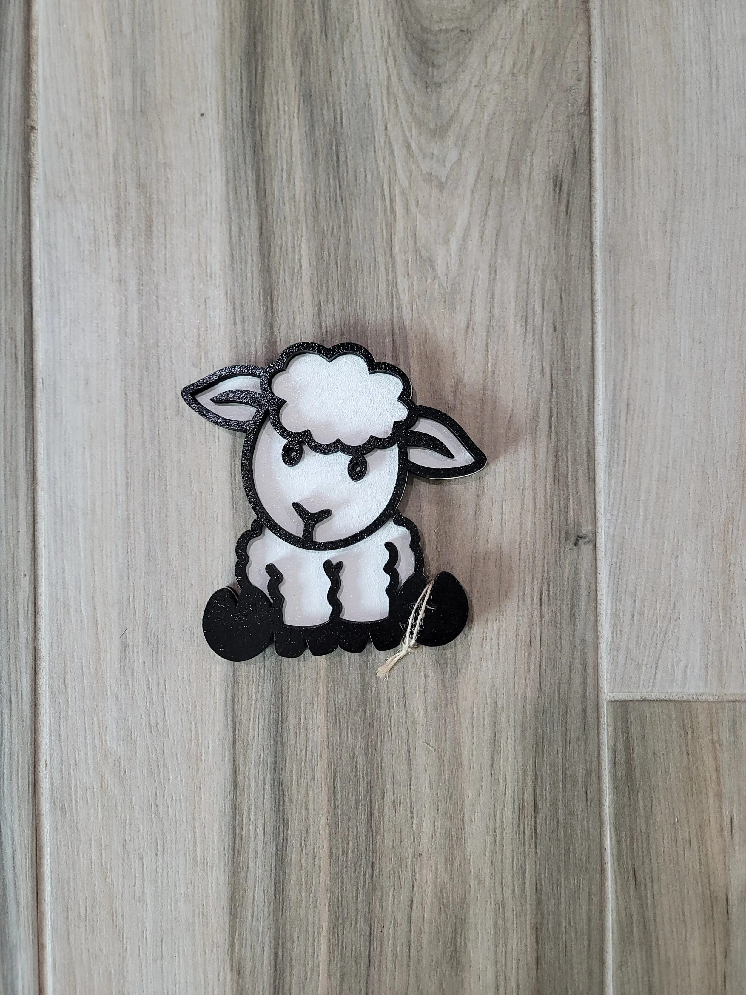 A decorative ornament resembling a cartoon sheep with a fluffy white face and body, black outline, and black feet.