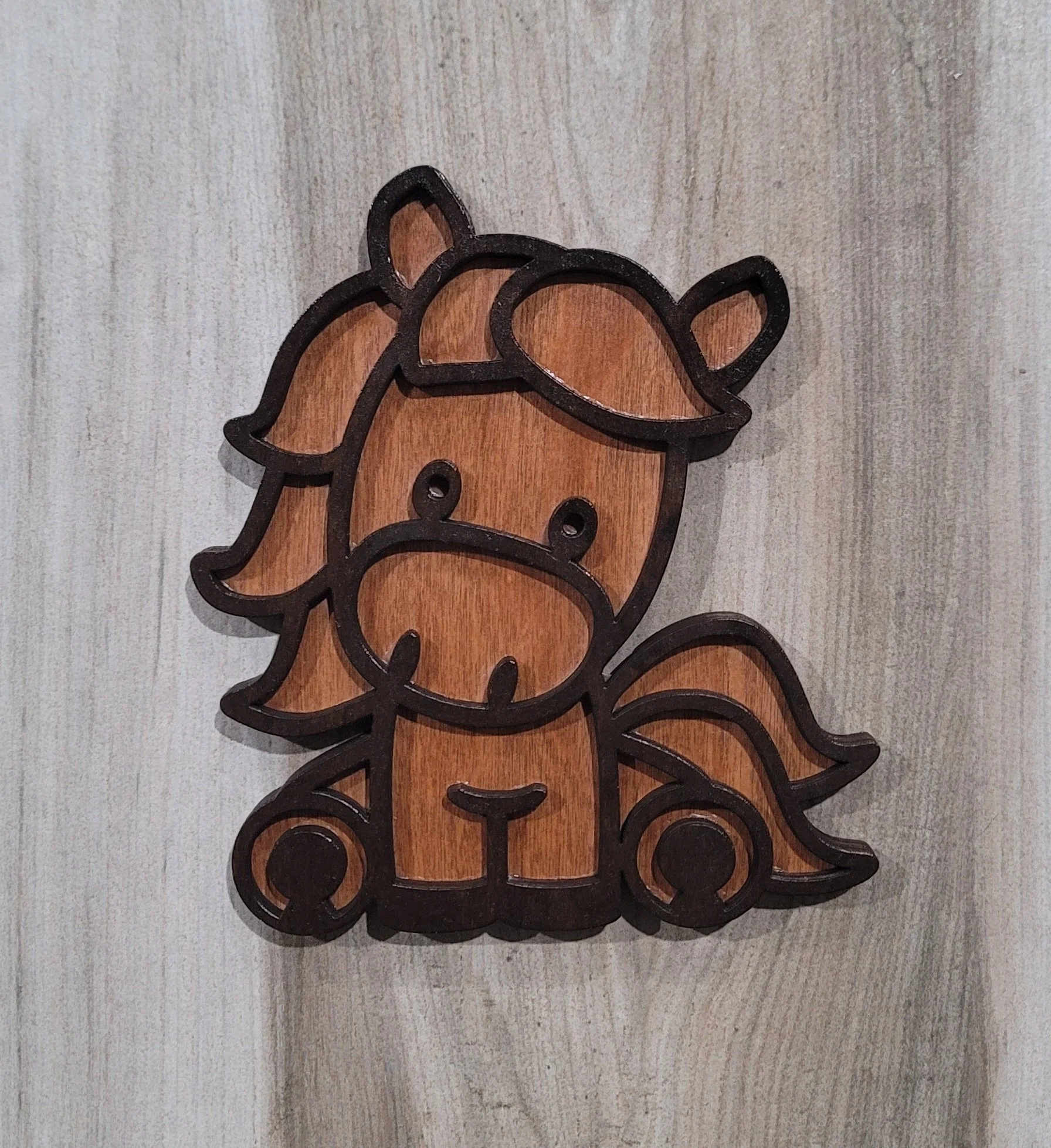 Wooden decorative piece of a cartoon-style horse with large eyes and a flowing mane, outlined in black.