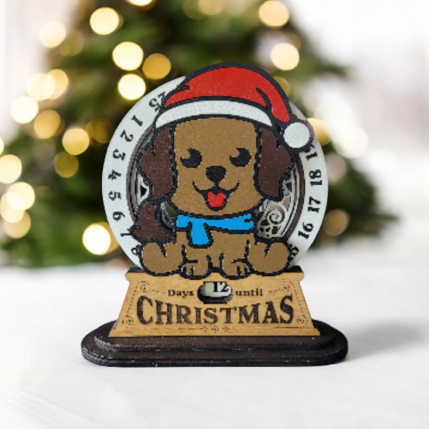 A decorative dog figure wearing a red Santa hat and a blue scarf, with a wreath background, and a wooden plaque indicating 12 days until Christmas.