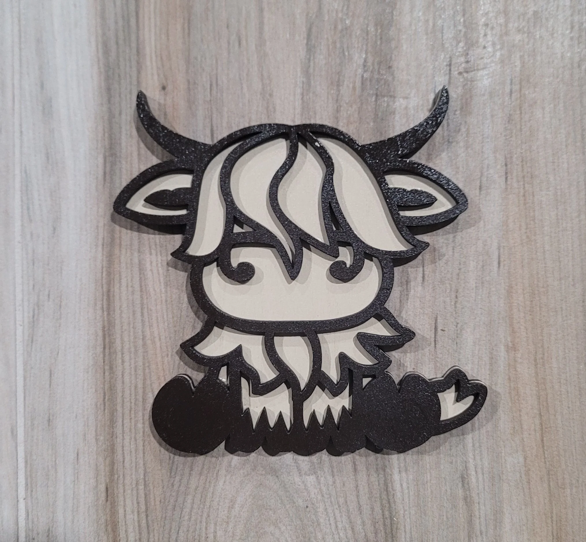 Decorative black outline of a cartoon cow with long hair, horns, and hooves