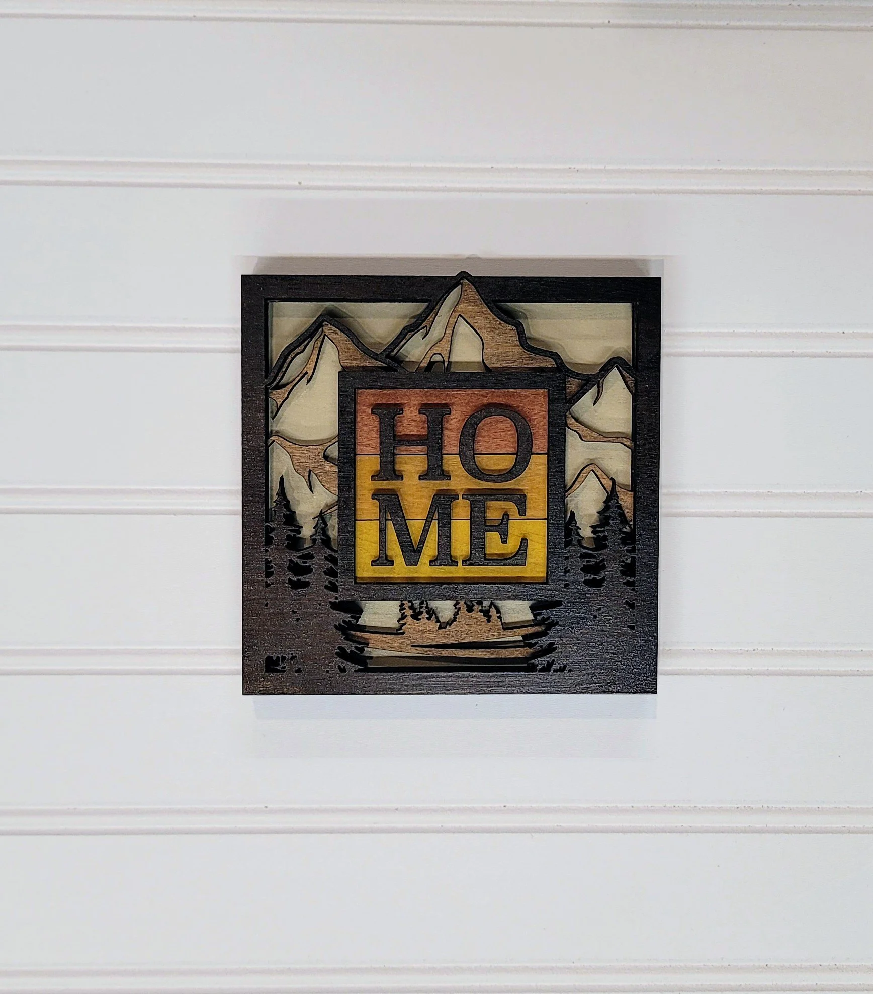 Decorative wall art with a mountain scene and the word 'HOME' in the center.
