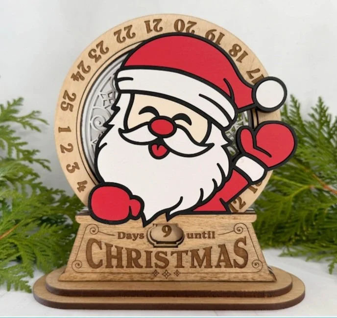 A wooden Christmas countdown calendar featuring a cheerful Santa Claus with a red hat, waving and smiling, with a greenery background.