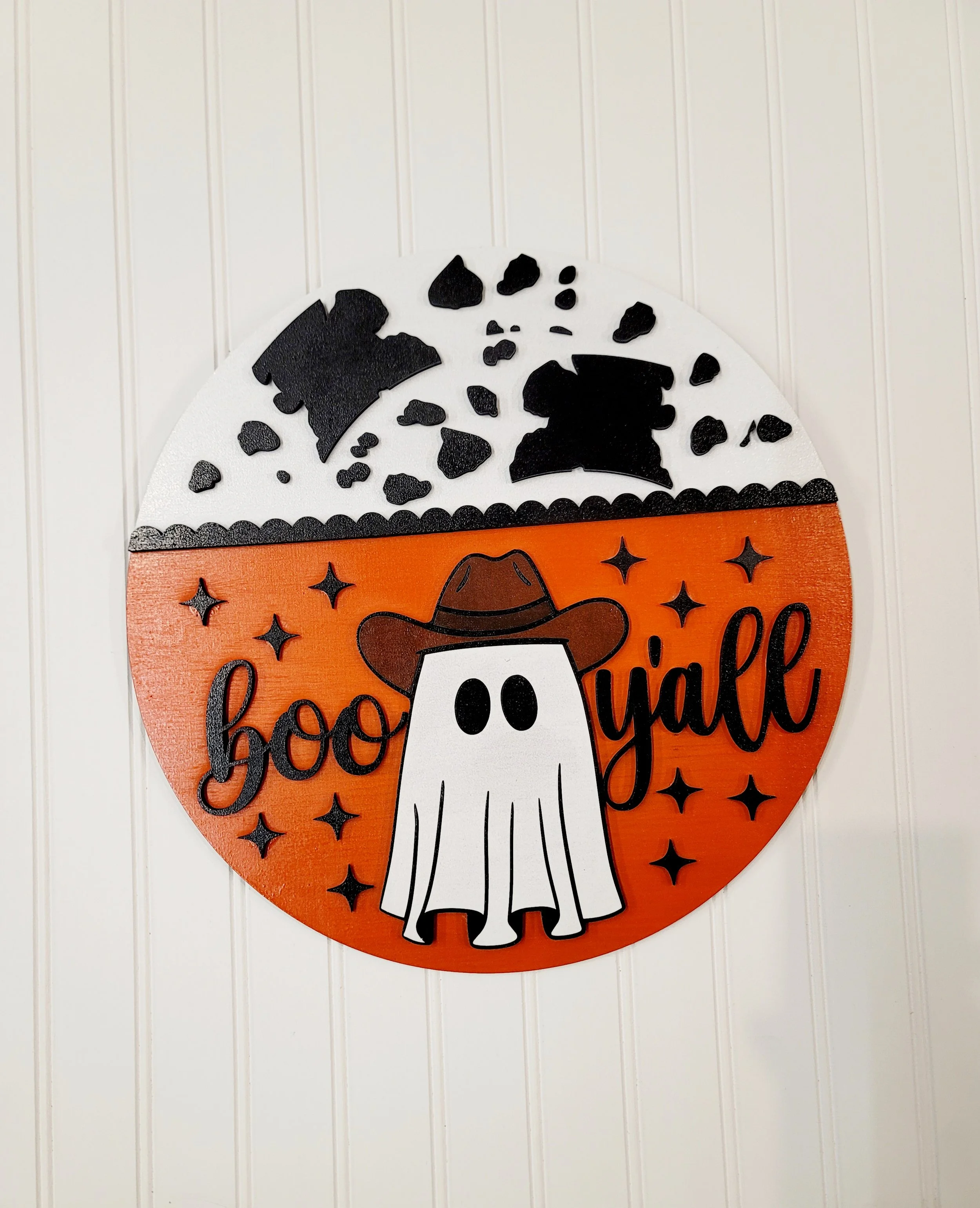 Halloween decoration with a ghost wearing a cowboy hat, the words 'boo y'all', and a background of black and white cow print.