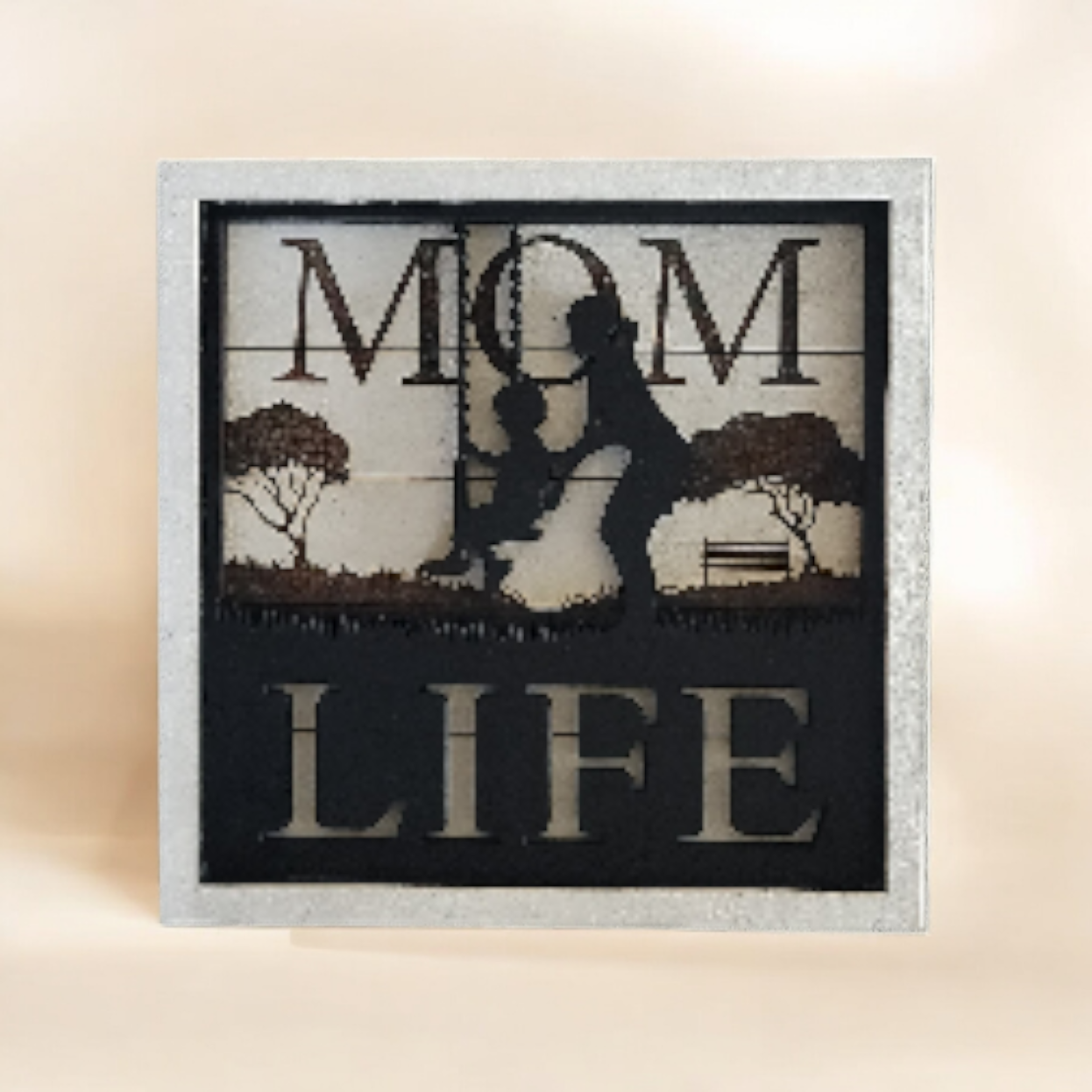 Silhouette of a woman holding a child on a swing with trees and a bench in the background, surrounded by the words 'Mom Life'.