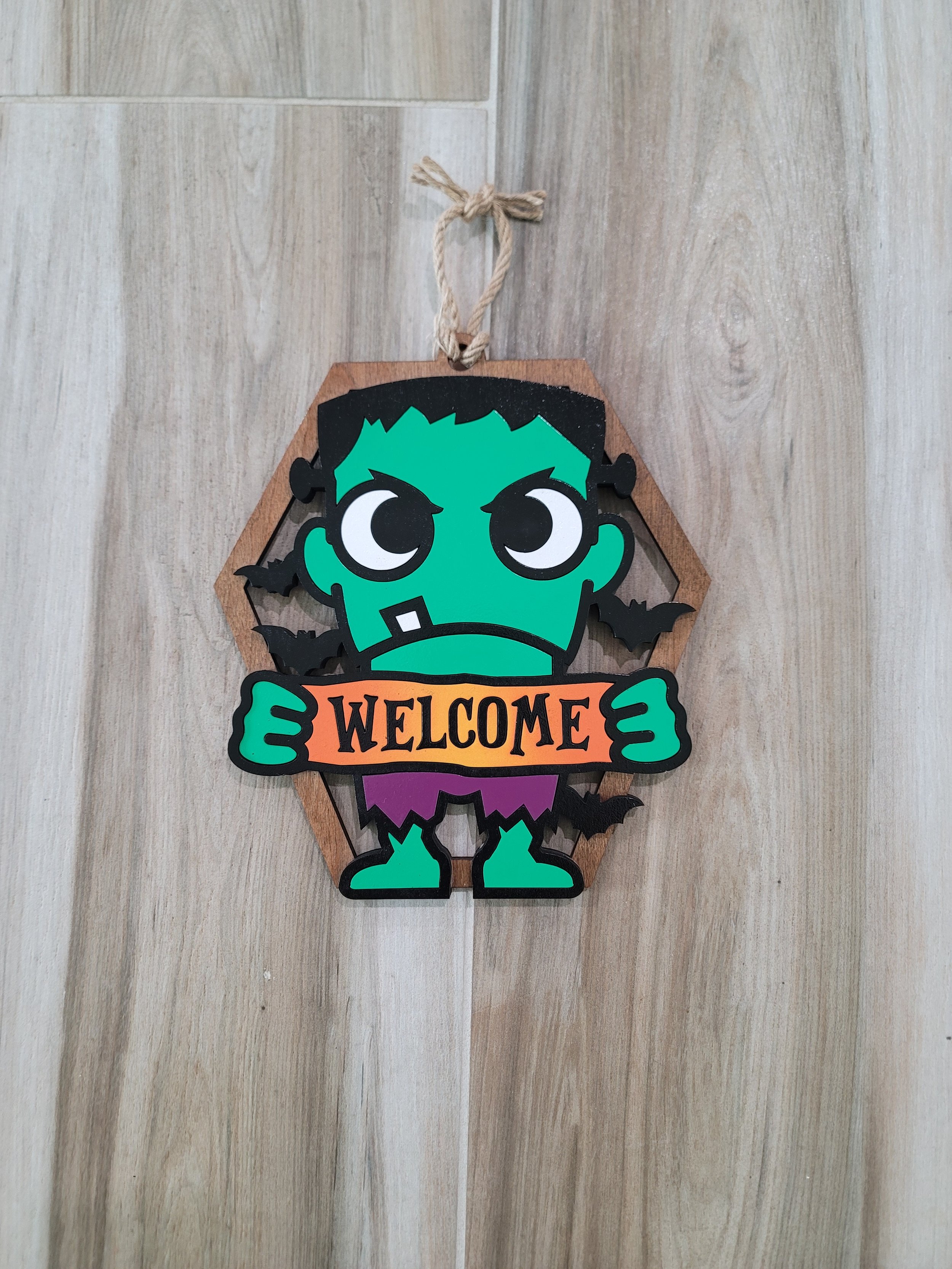 Halloween decoration featuring a cartoon Frankenstein holding a sign that says 'WELCOME', with black bats around it