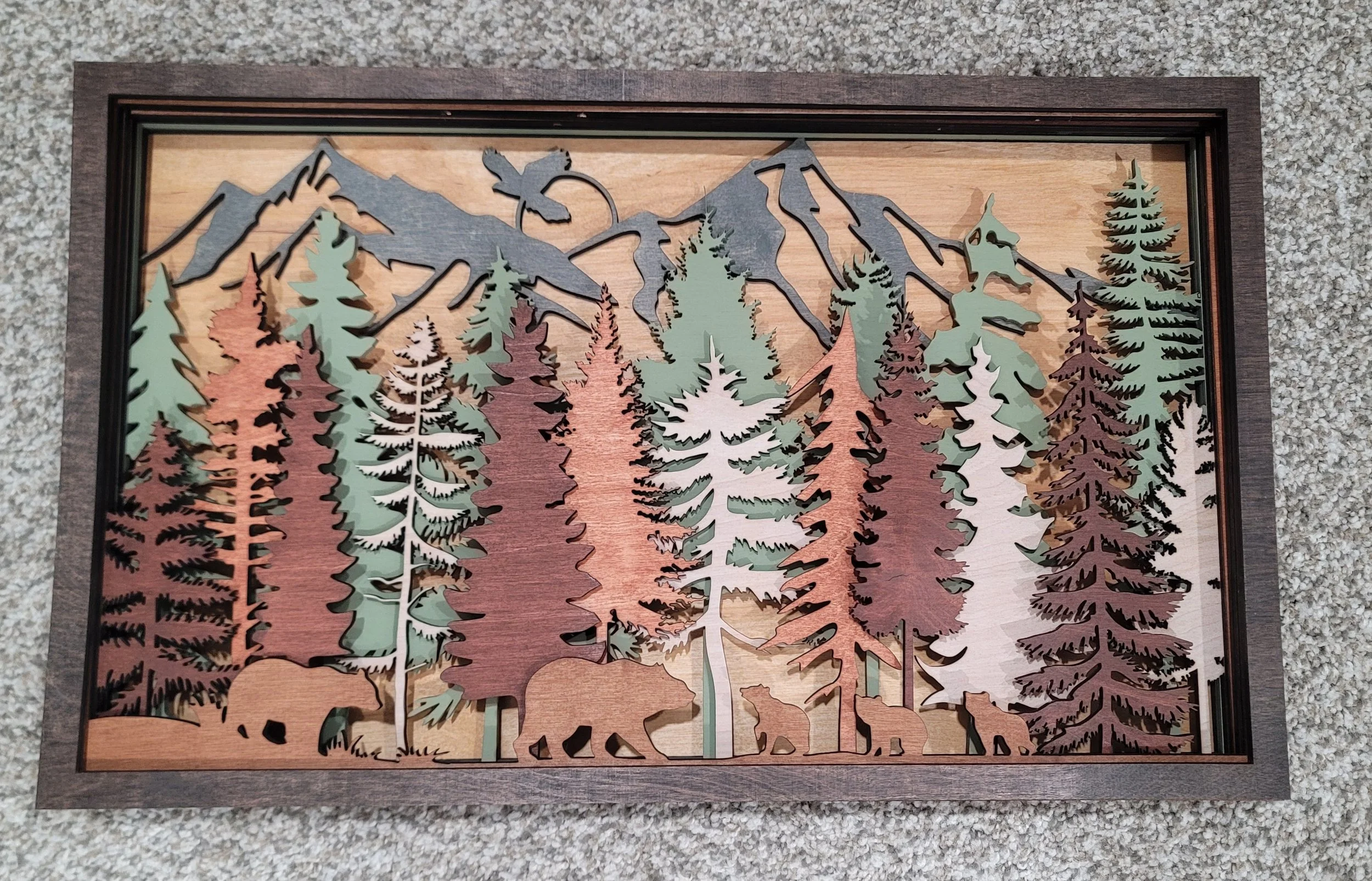 Wooden framed metal art of a mountain landscape with trees, bears, and a bird in flight.