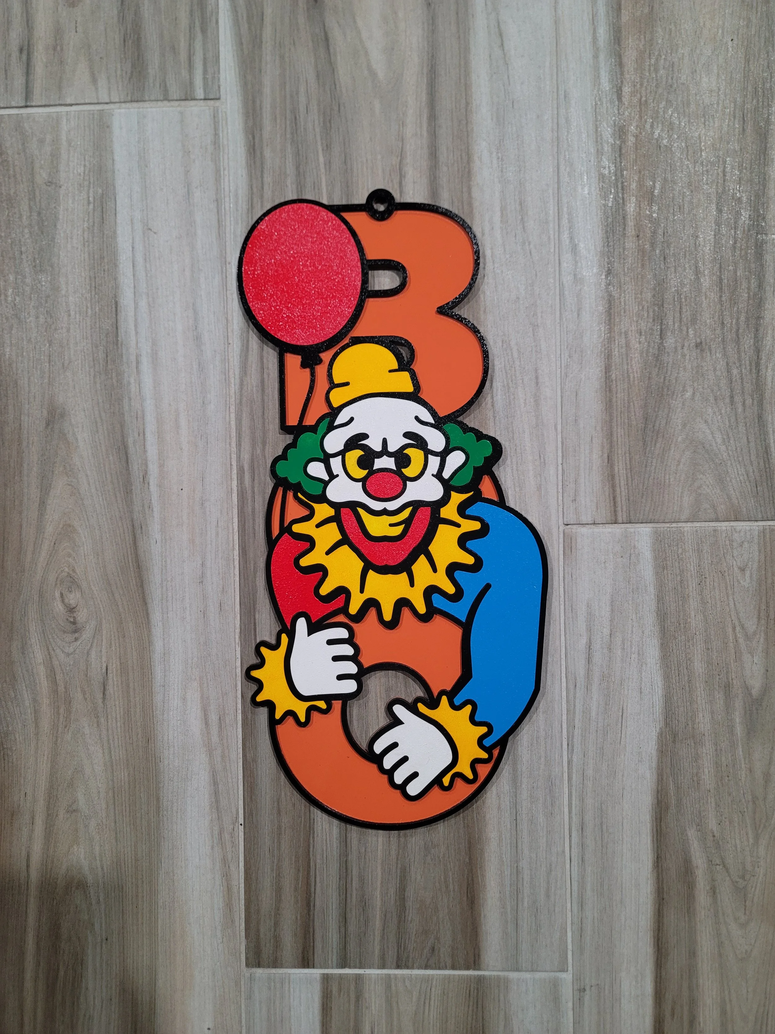 A colorful Halloween decoration featuring a creepy clown figure with a red balloon, positioned over the wood BOO