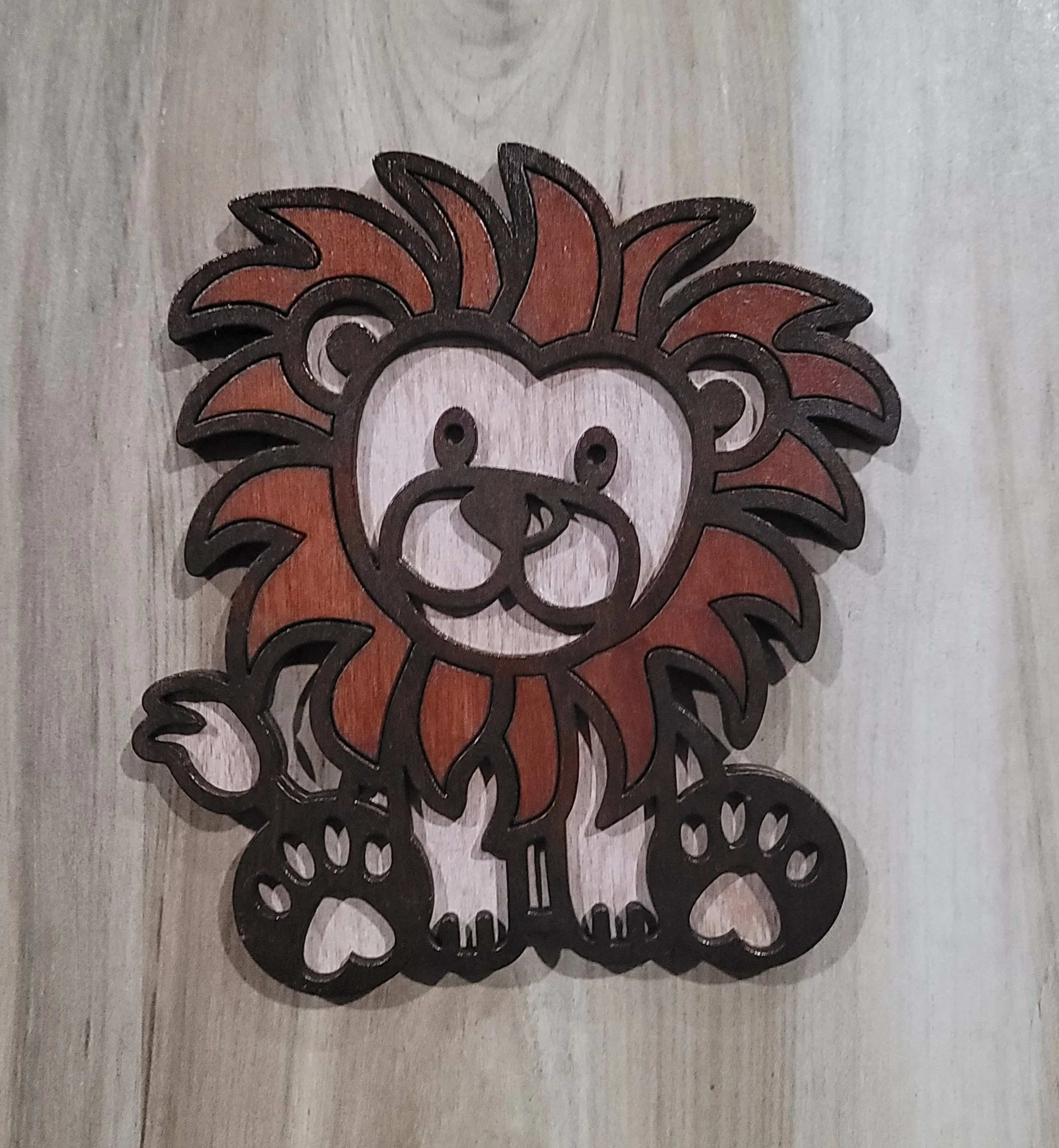 Wooden decorative piece of a cartoon lion with a mane, face, paws, and tail, painted with brown, beige, and black colors