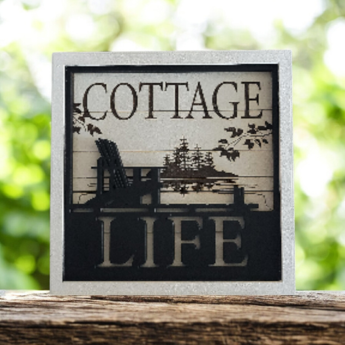 Decorative sign with the words 'Cottage Life' and an illustration of a porch with a chair, trees, and branches.