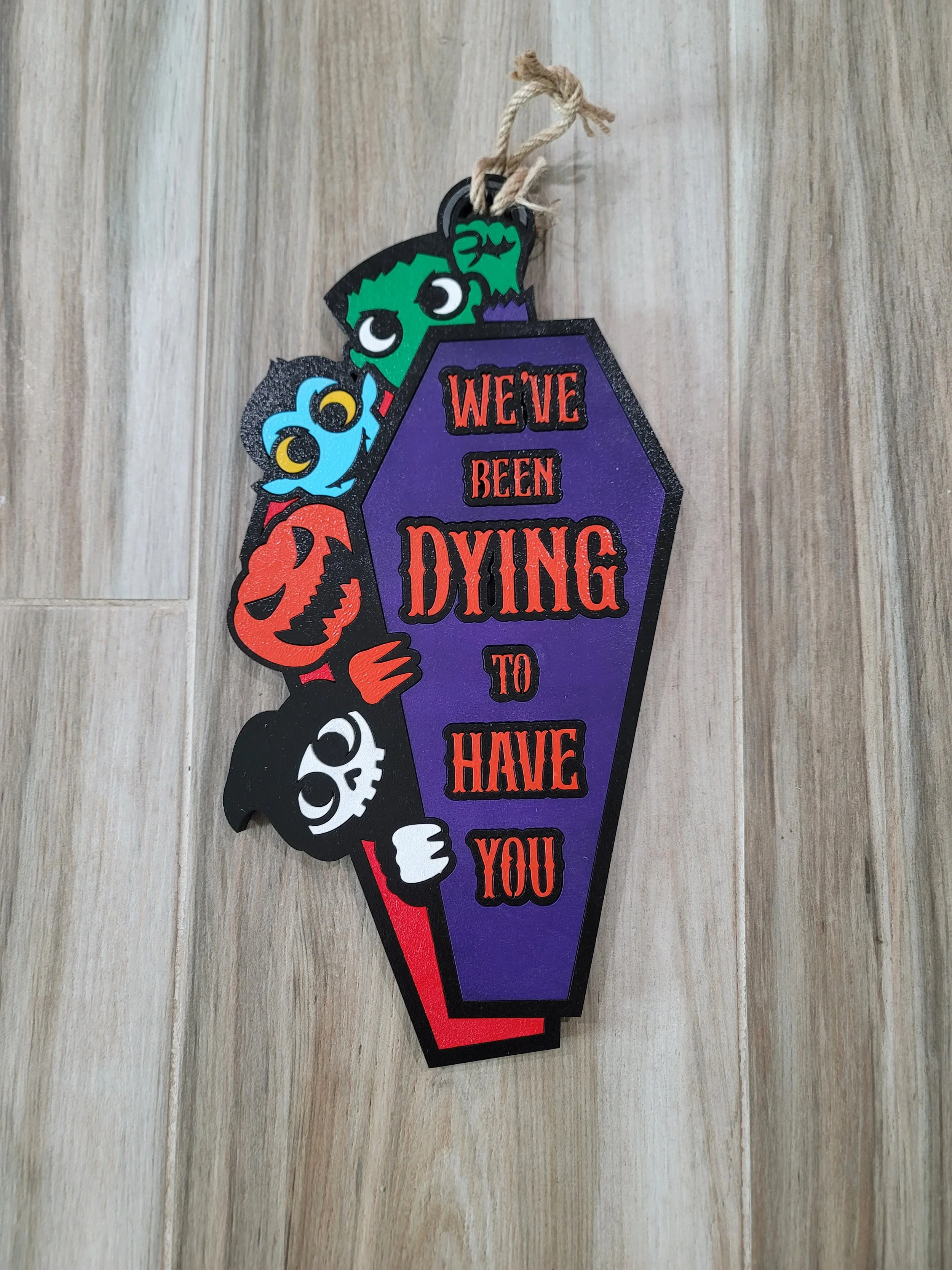 Halloween-themed door hanger with cartoon ghosts and a purple coffin shape, displaying the message 'We've been dying to have you' in red and black text.