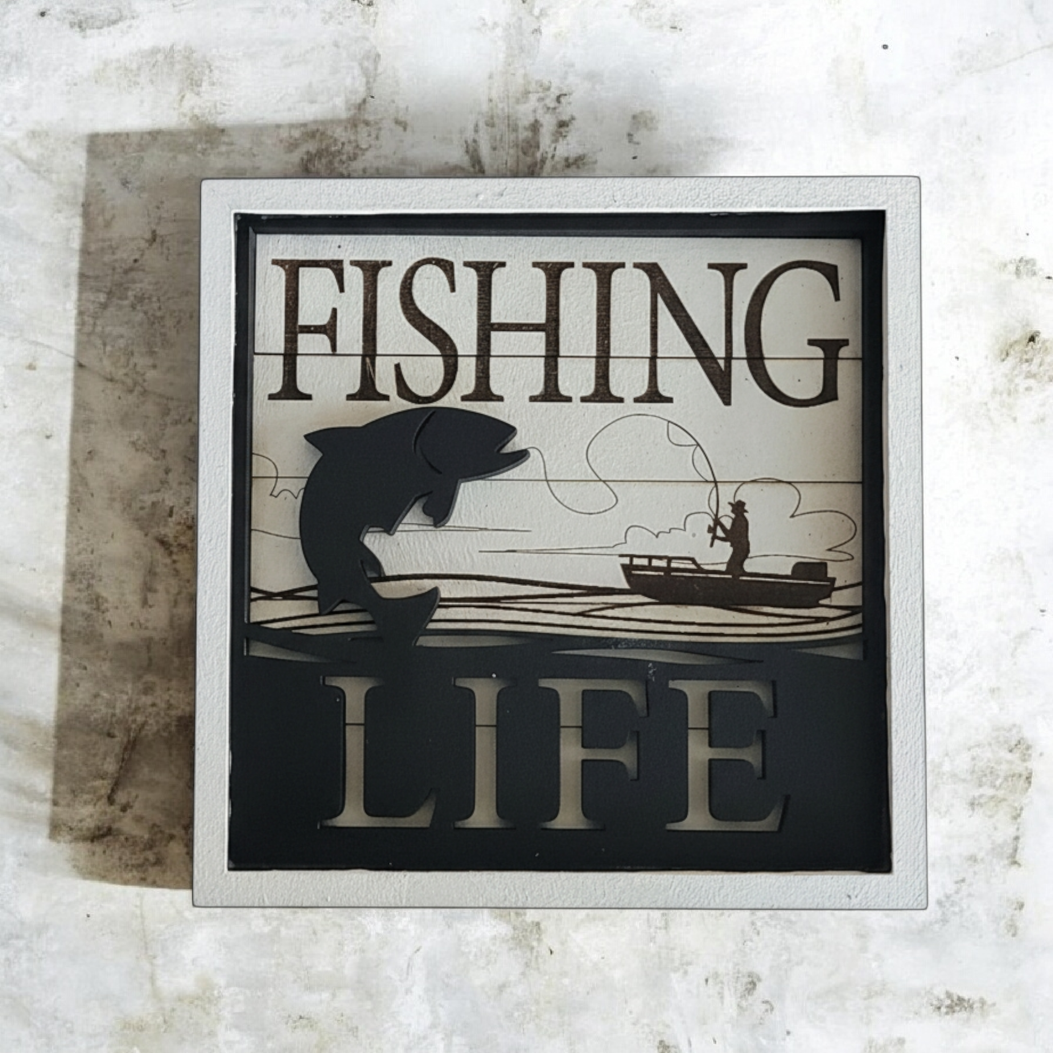 Decorative sign with the words "FISHING LIFE" and images of a fish, a fishing line, and a person fishing from a boat.