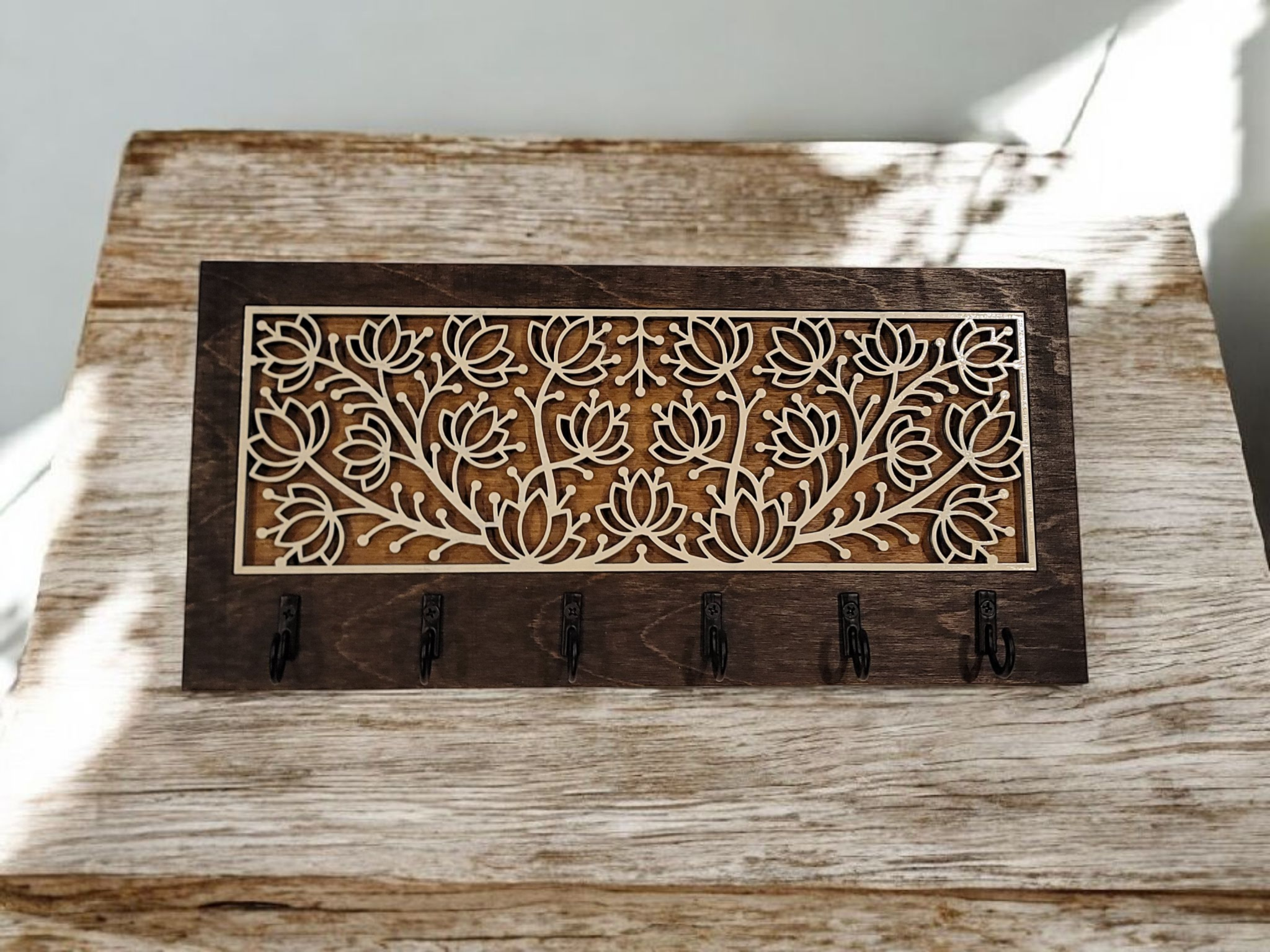 A wooden key holder with a decorative carved panel featuring a floral pattern, mounted on a distressed white wooden surface.