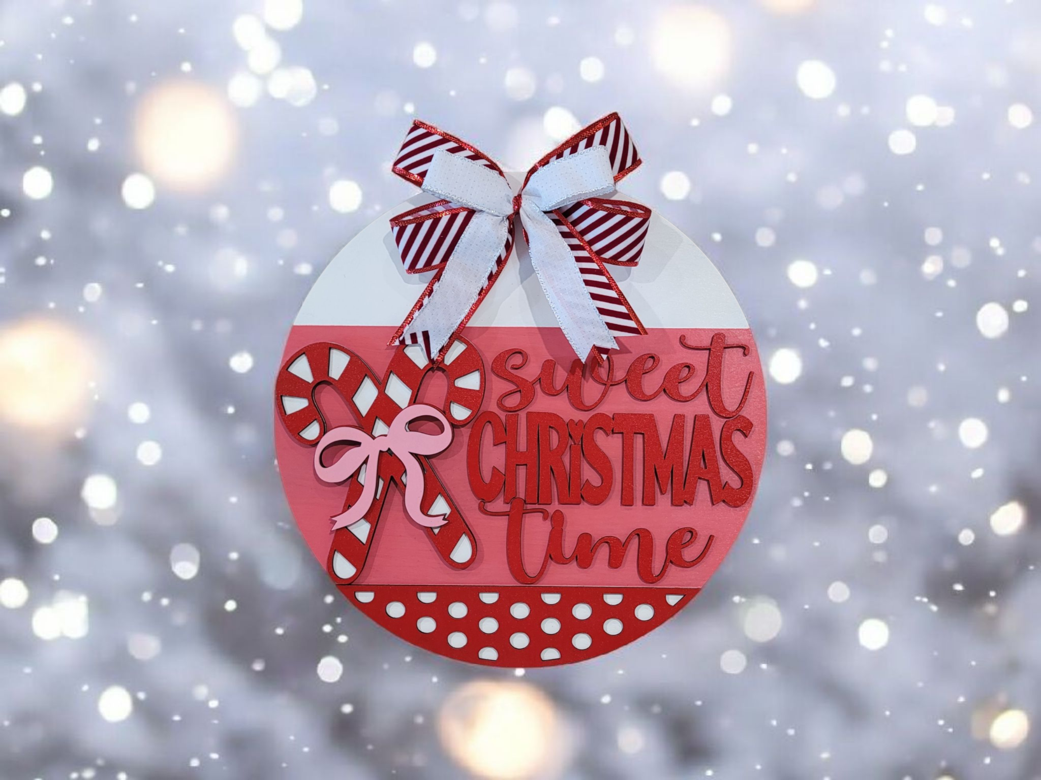 Round Christmas ornament with red and white striped bow, pink glittery candy canes, and the words "sweet Christmas time" on a snowy background.