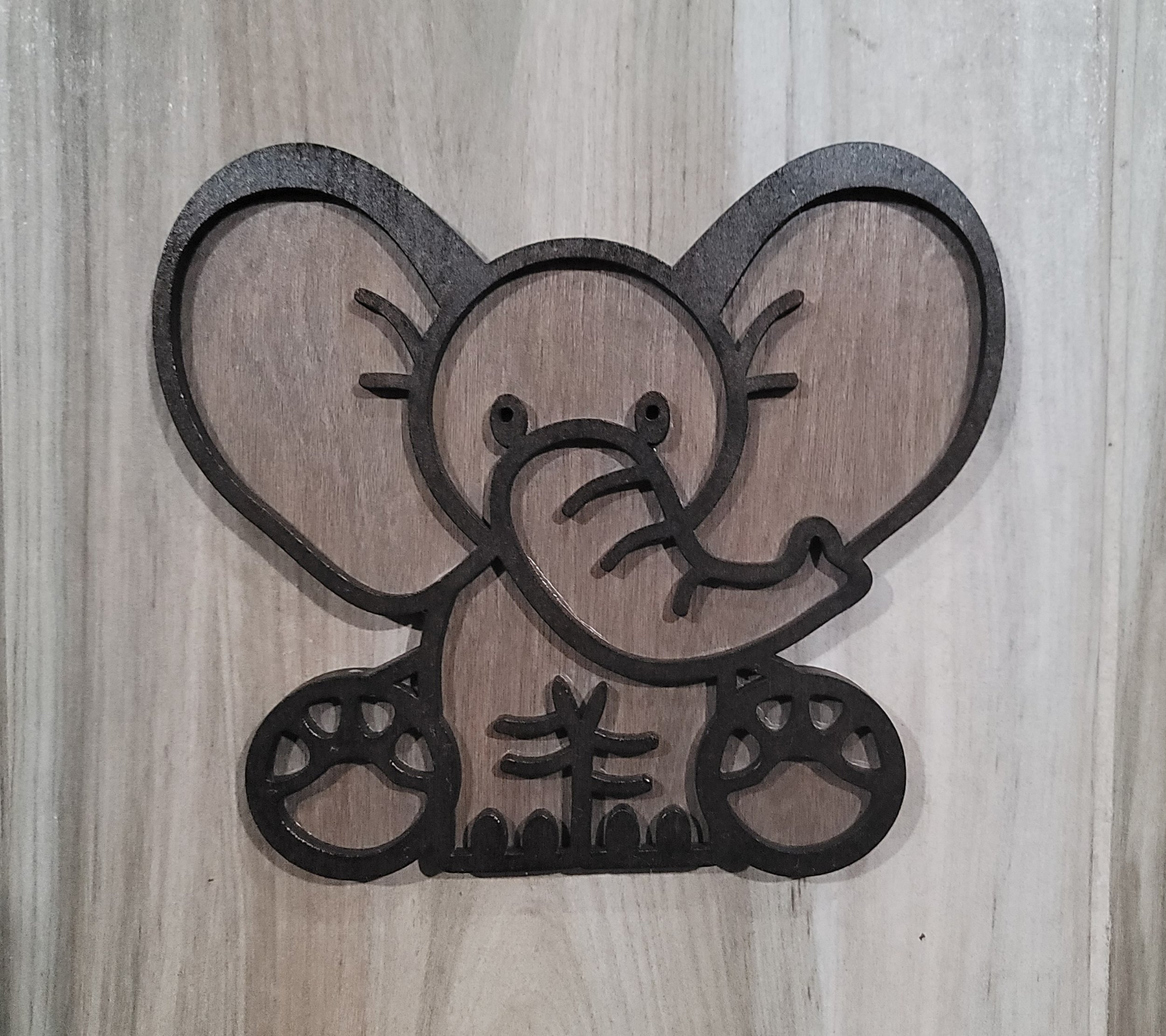 Decorative wooden cutout of a cute cartoon baby elephant with large ears, small eyes, a trunk, and paw prints on its feet
