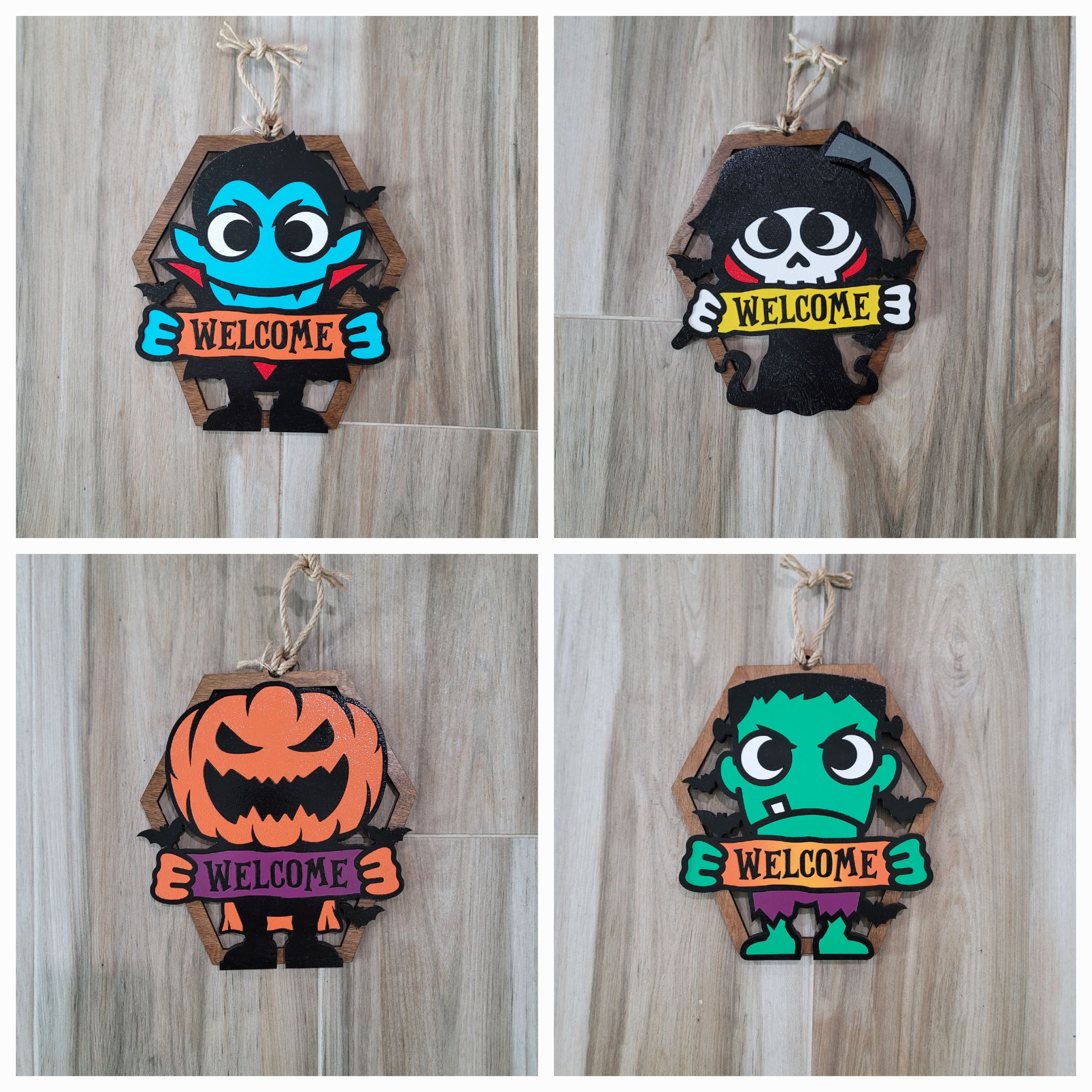 Four Halloween-themed hanging decorations featuring cartoon monsters and a jack-o'-lantern, each holding a 'WELCOME' sign, displayed on a wooden surface.