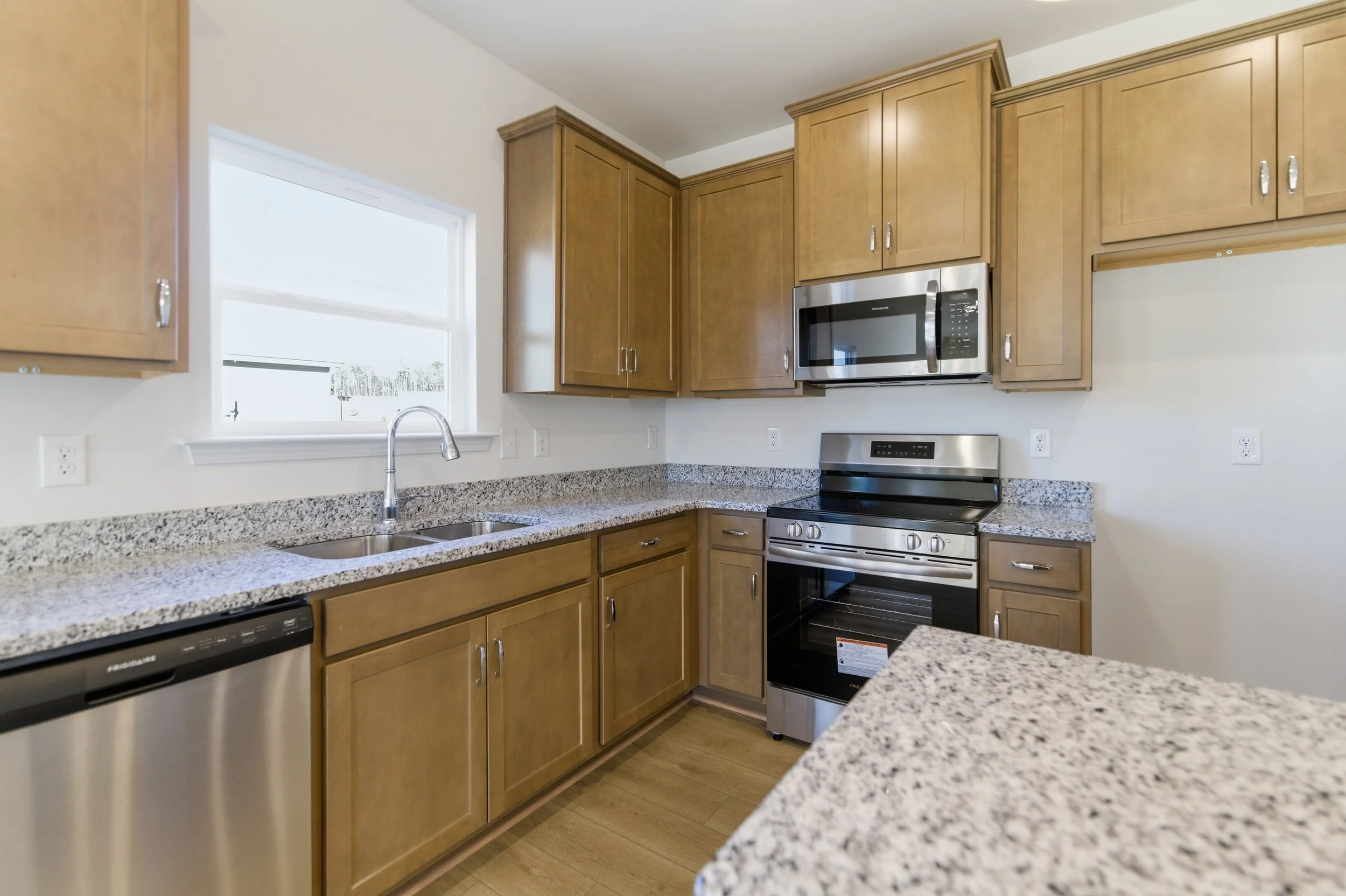 Kitchen with wooden cabinets, granite countertops, stainless steel appliances including an oven, microwave, and dishwasher, and a window above the sink.