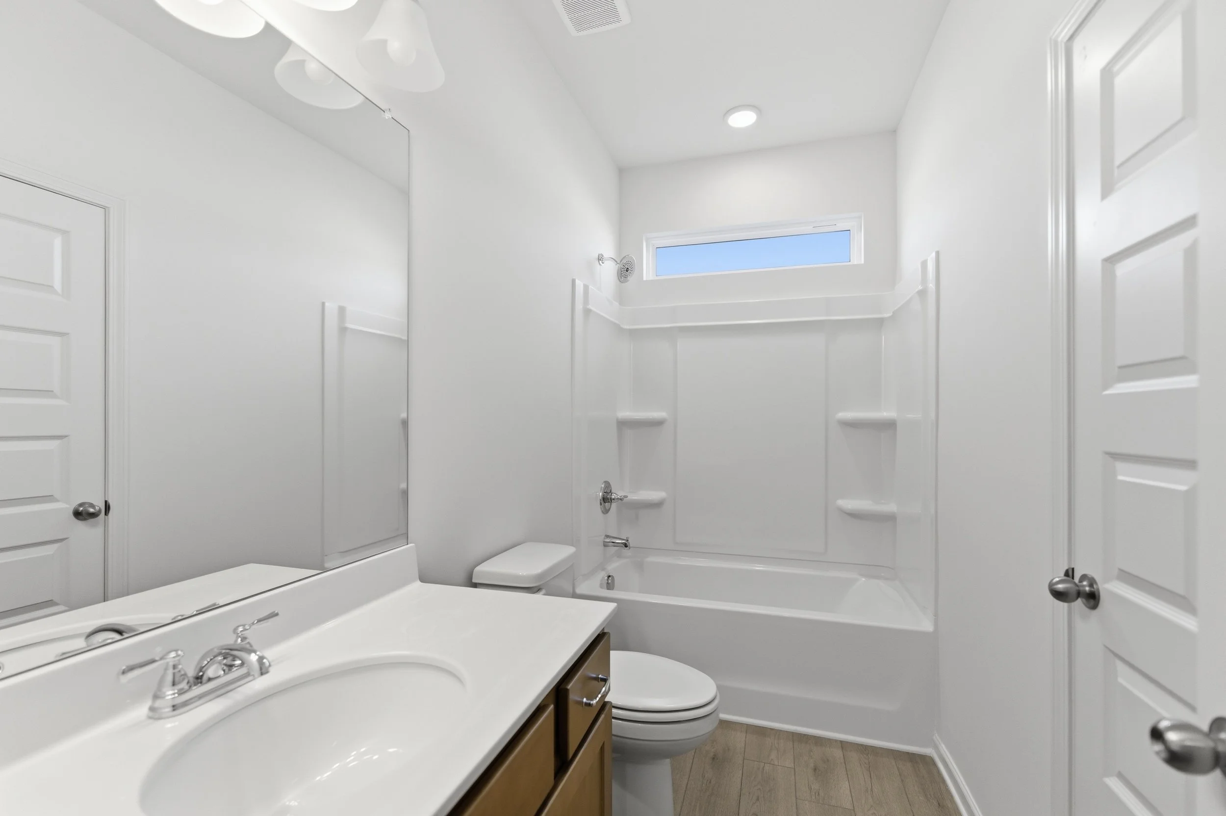 Empty white bathroom with bathtub, toilet, vanity with mirror, and small horizontal window