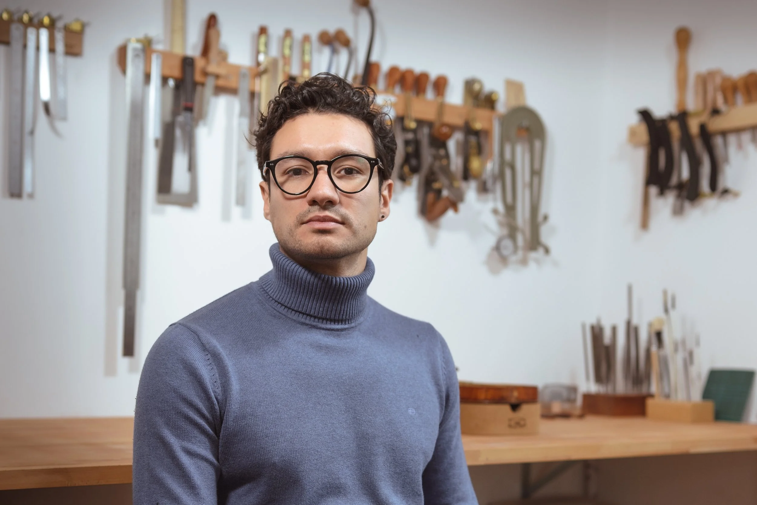 Mann steht in einer Werkstatt vor einer Werkbank mit Werkzeugen an der Wand im Hintergrund