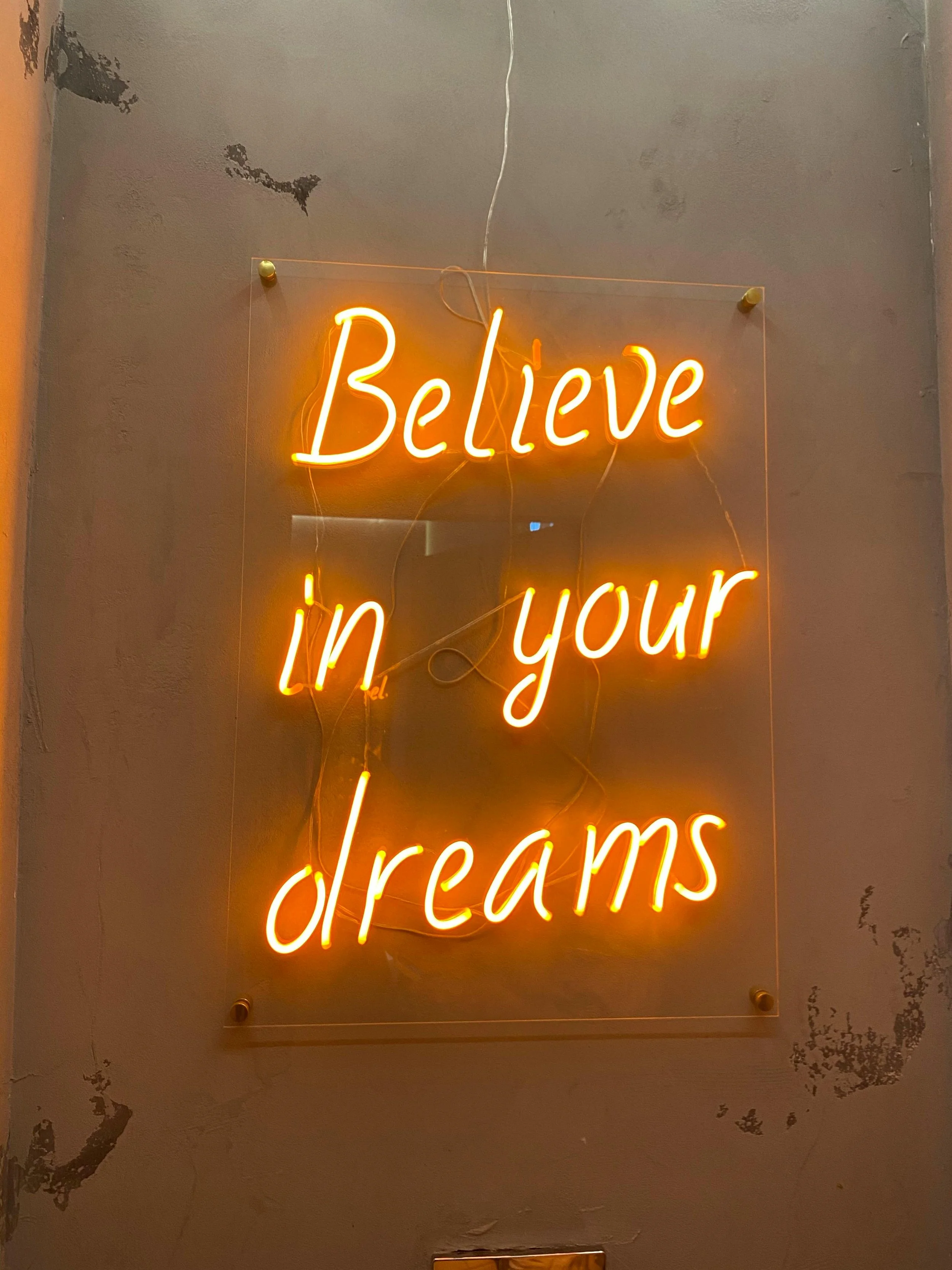 A neon sign on a wall that reads 'Believe in your dreams' in orange light.