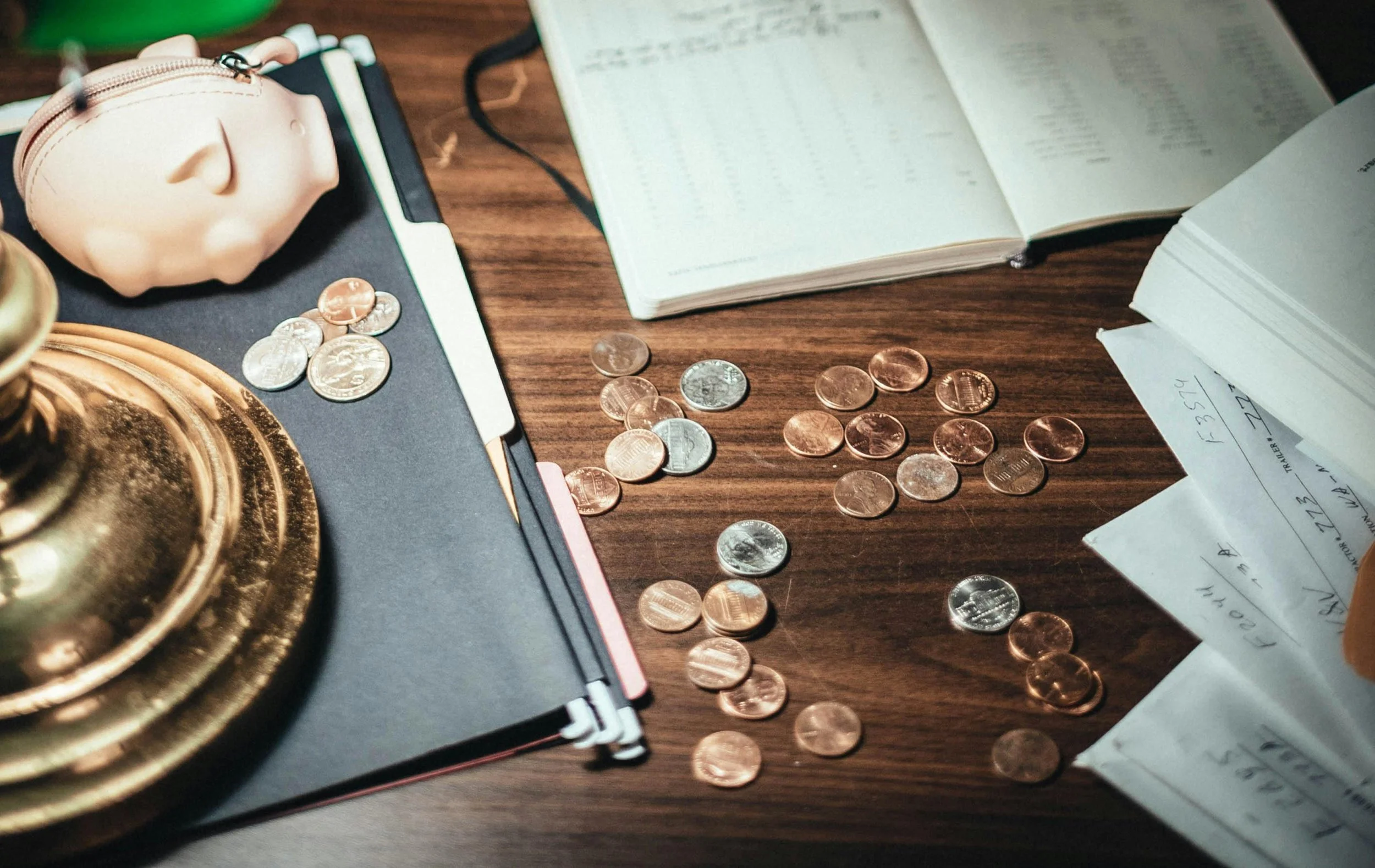 Spilled coins, open notebooks, papers, and a pink coin purse on a wooden desk.