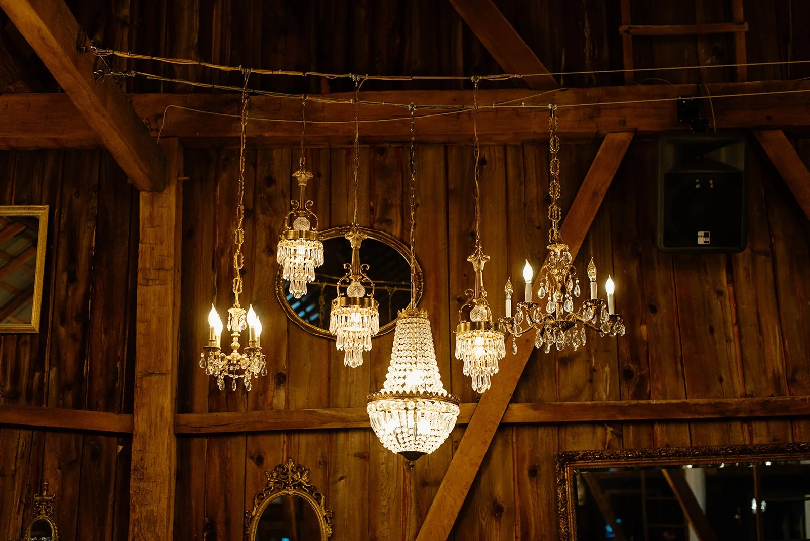 Multiple ornate crystal chandeliers hanging from a wooden ceiling in a rustic interior.