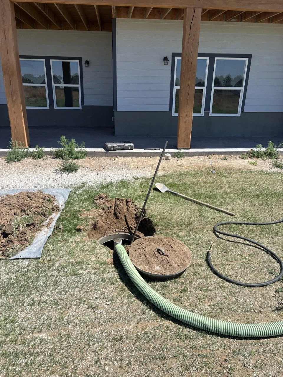 Digging a septic hole in the backyard for a septic tank, with construction tools and a house in the background.