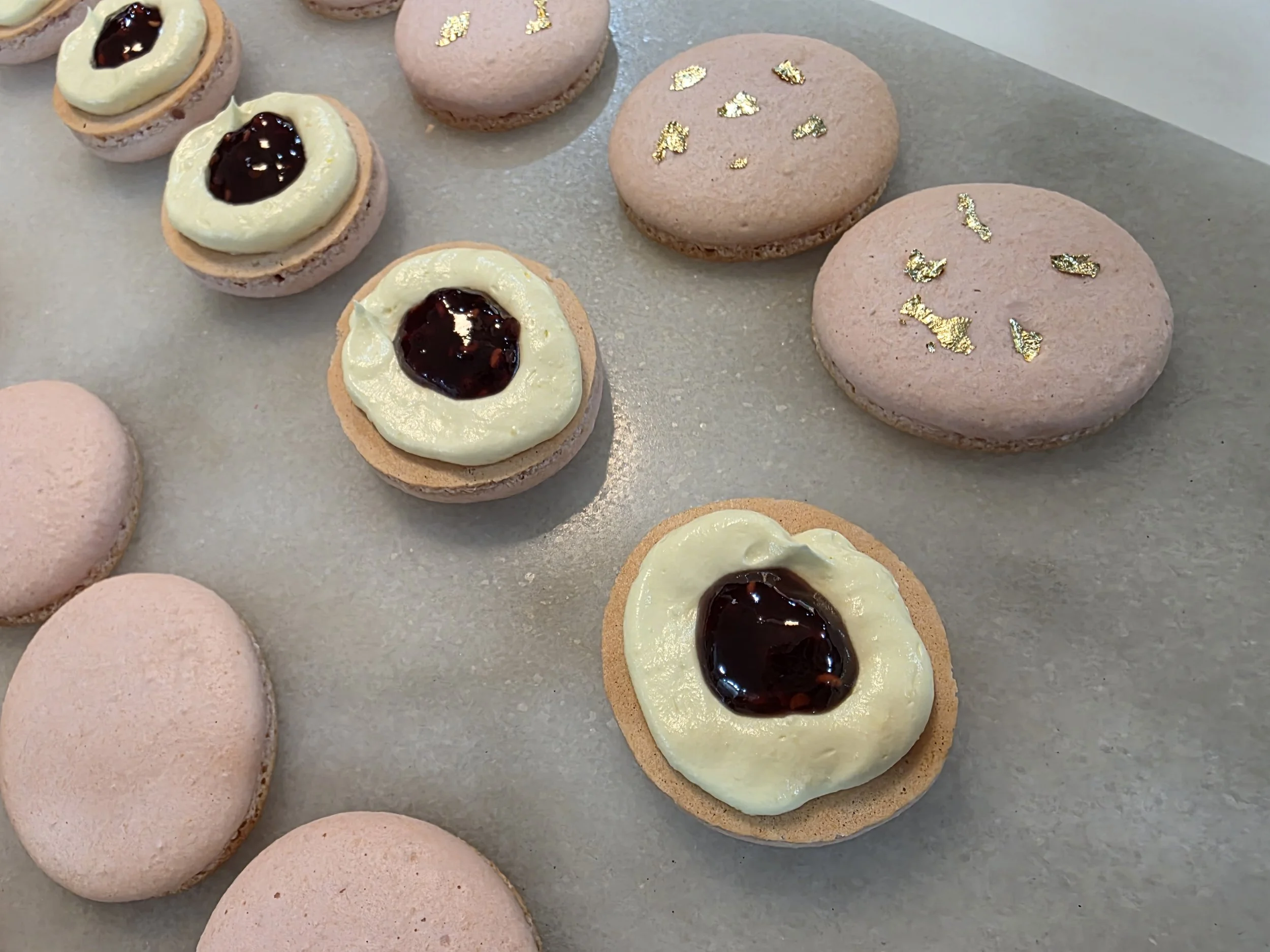 Pink rose water macarons with buttercream and raspberry preserves filling, topped with edible gold leaf.