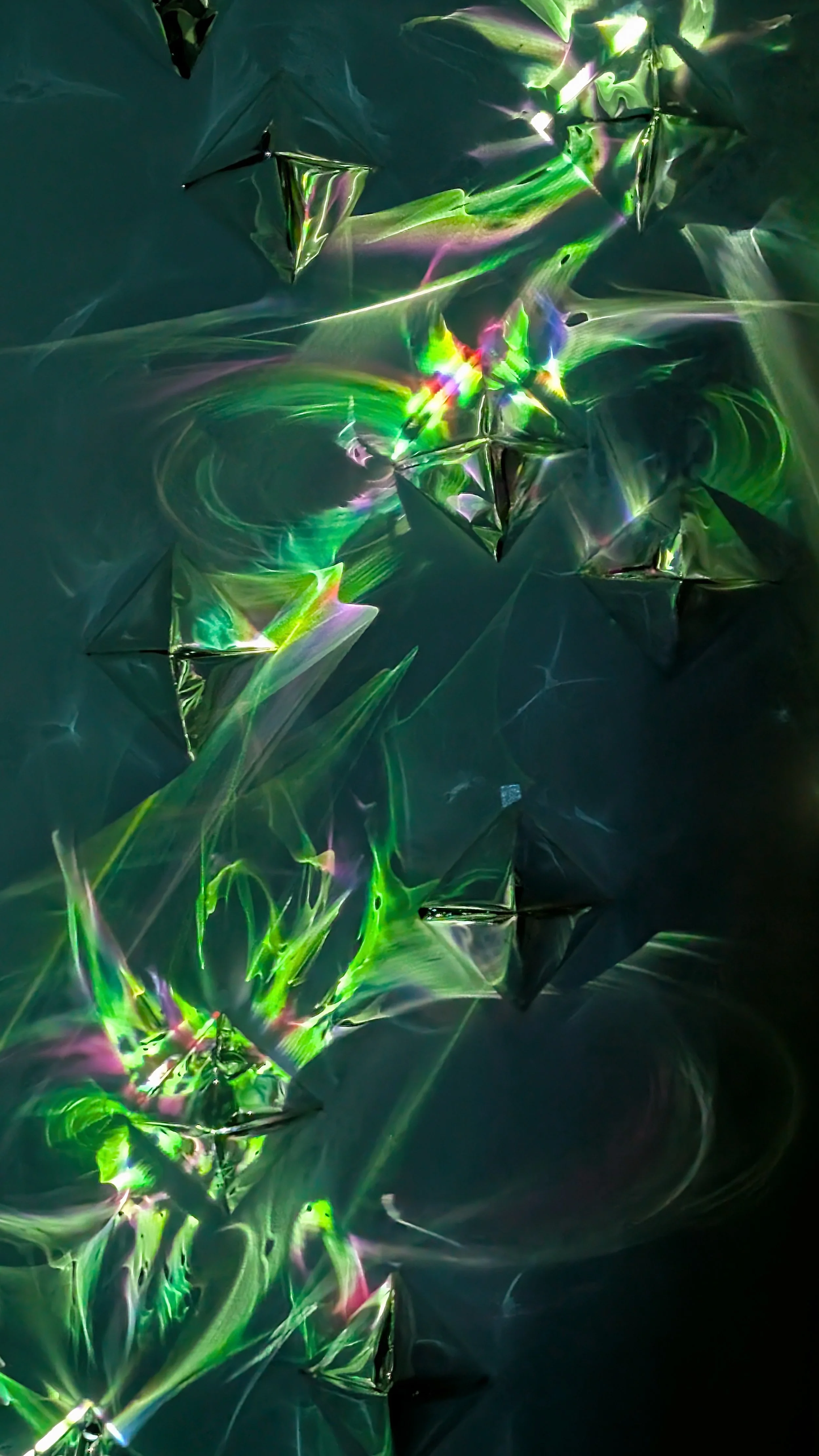 Abstract digital art with sharp, reflective, pyramid-shaped structures, swirling light patterns, and vibrant colors including green, purple, and rainbow hues.