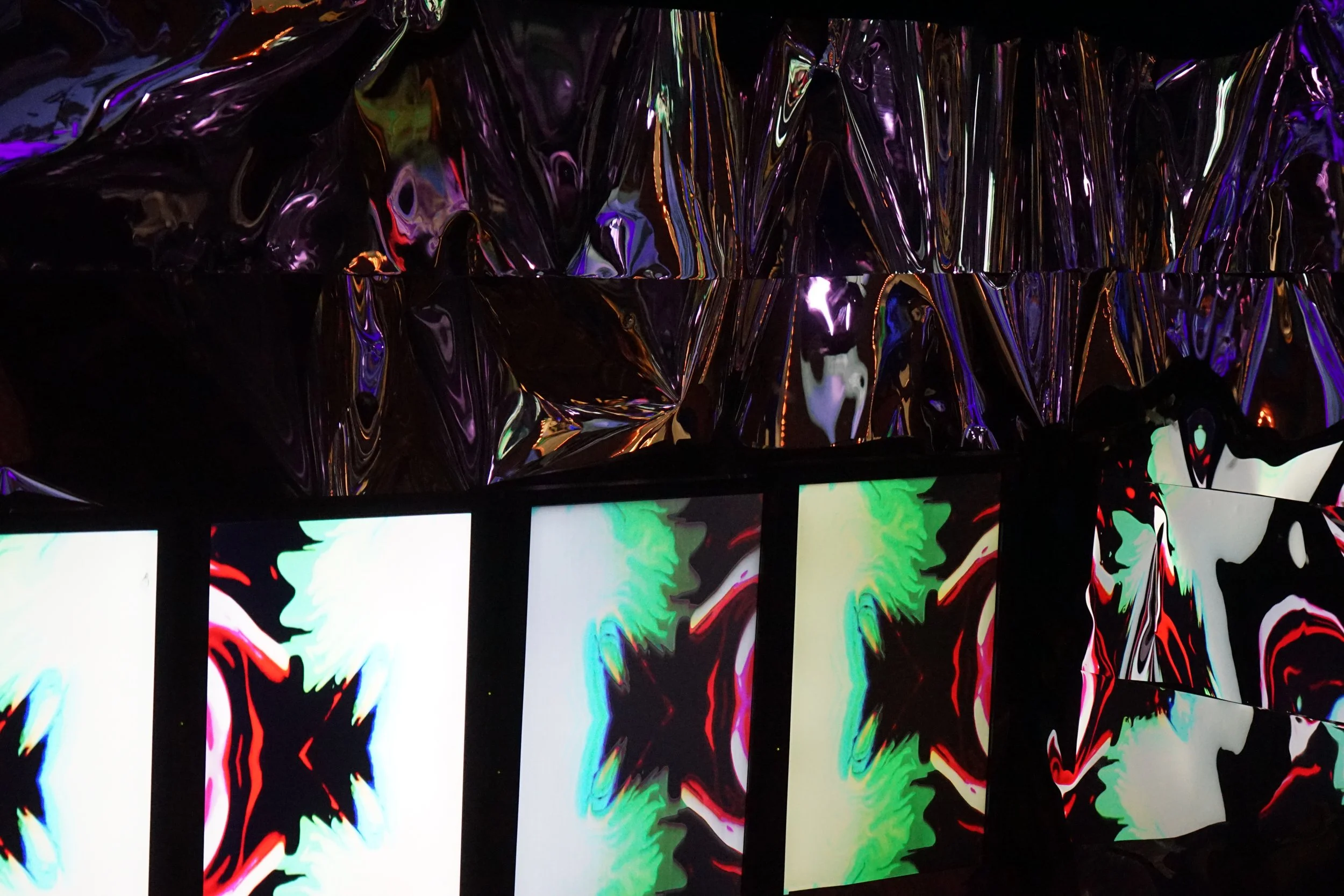 Colorful, abstract display with illuminated screens showing star-shaped patterns and a reflective, metallic surface above.