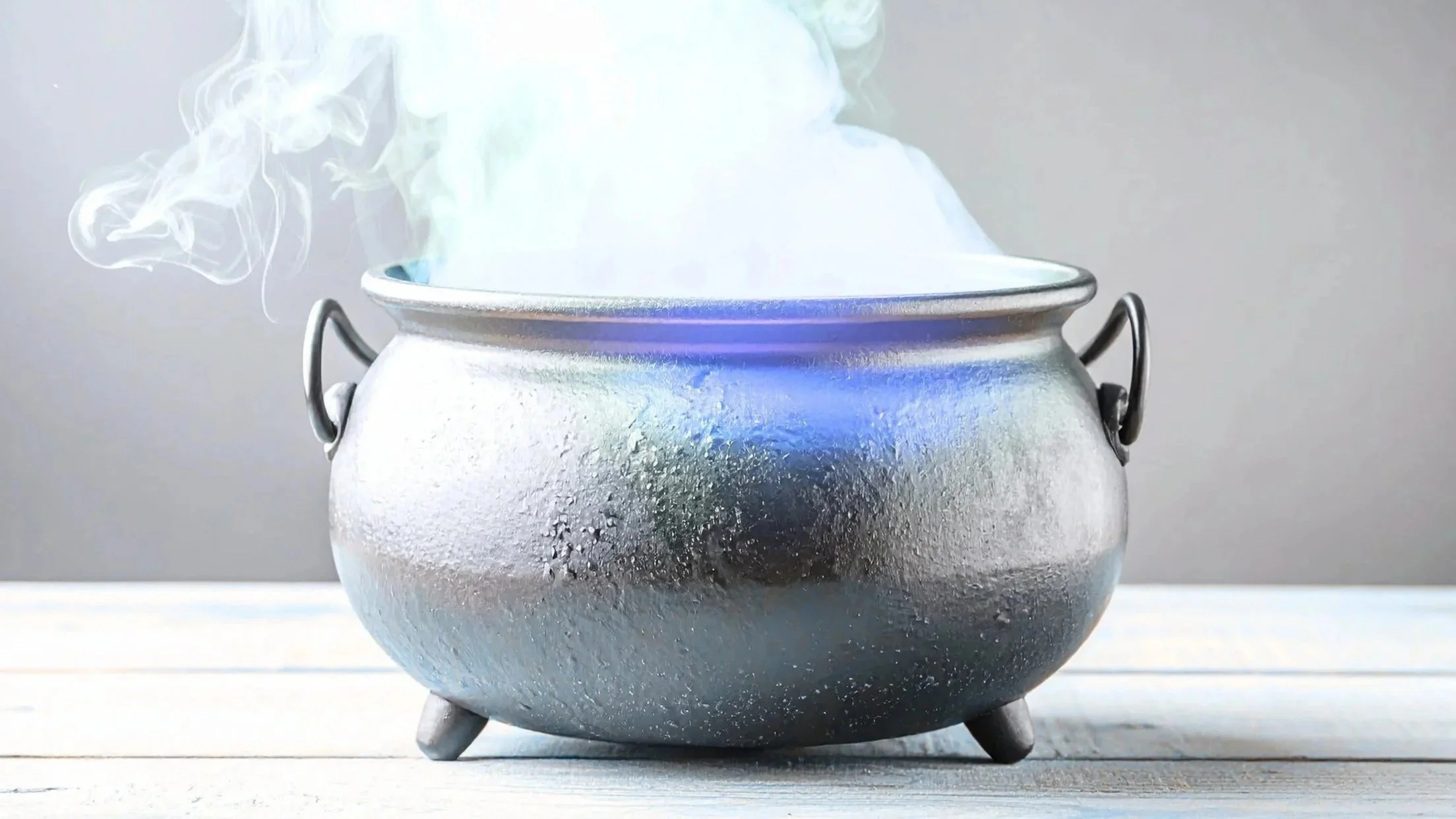 A metal cauldron with steam rising from it, placed on a white wooden surface.