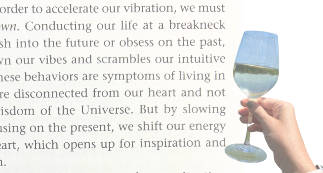 A hand holding a glass of white wine in front of a printed passage about slowing down, with a lake and sky scene visible through the wine glass.
