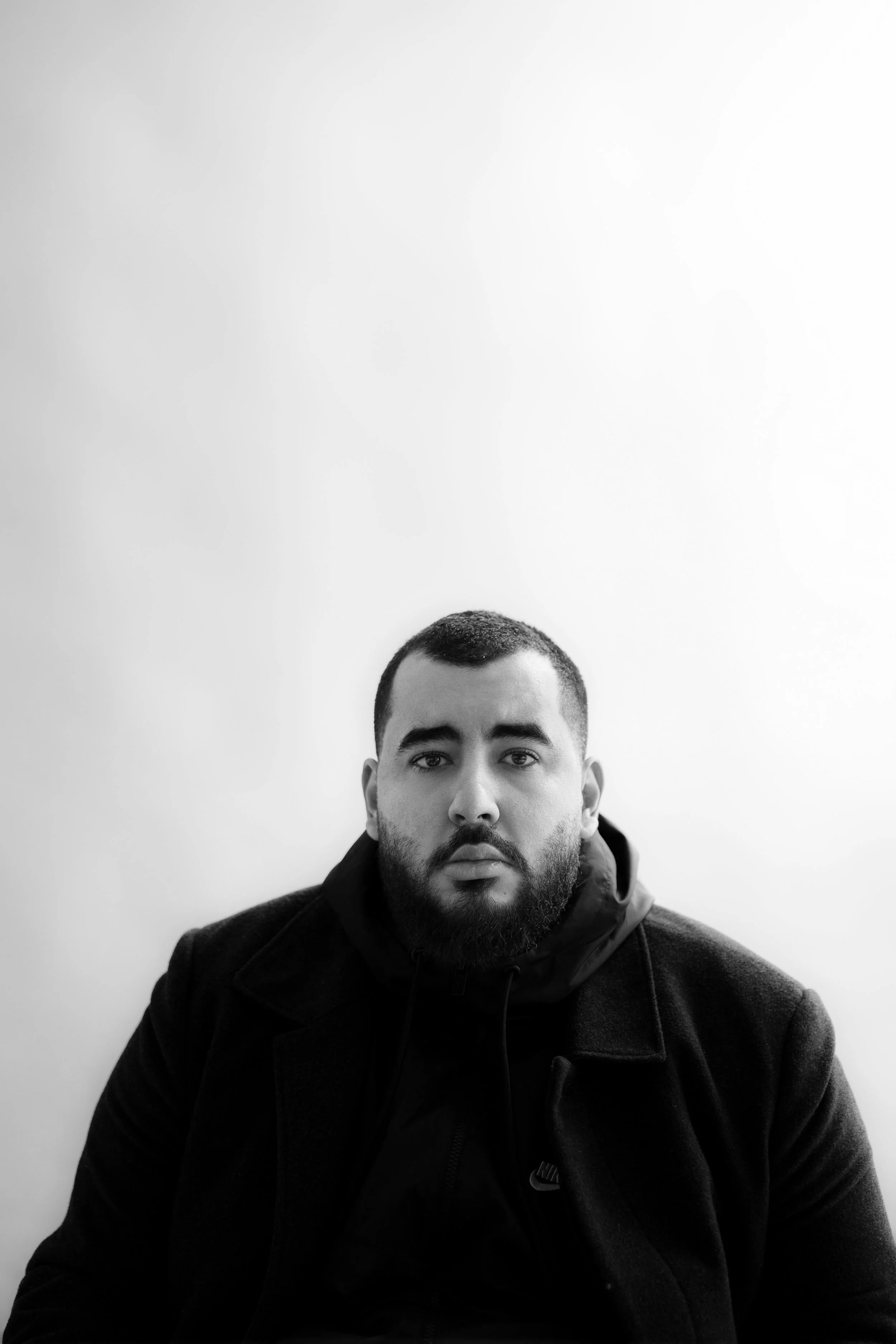 Portrait of a man with a beard and short hair, wearing a dark jacket, against a plain light background.