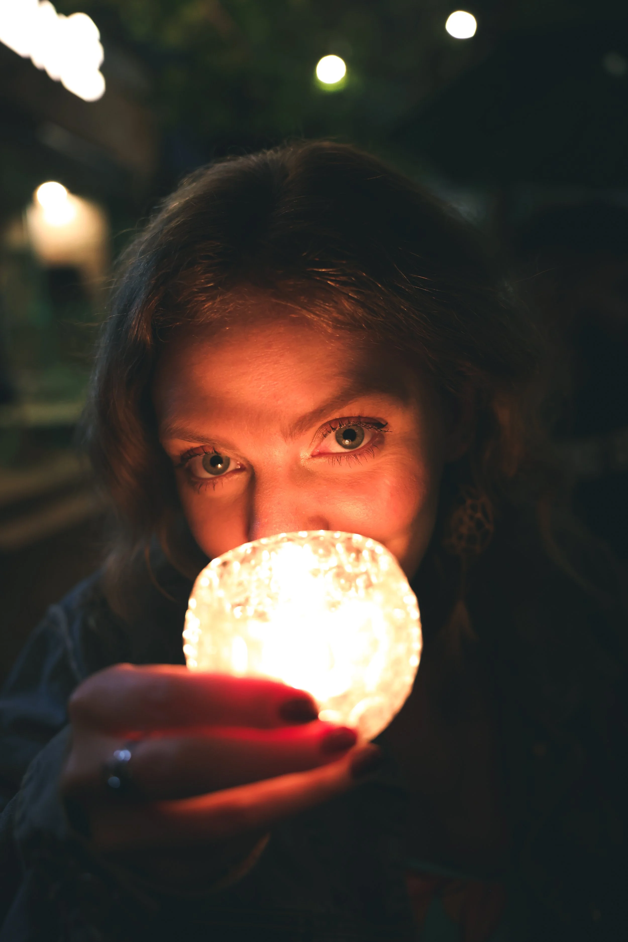 Person holding a glowing lamp close to their face in a dimly lit setting.