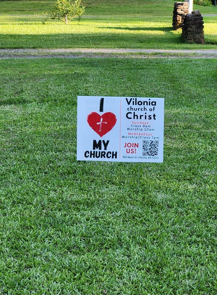 A sign placed on a grassy lawn advertising Vilonia Church of Christ services, with details about service times on Sundays and Wednesdays, a QR code, and a message encouraging joining the church.