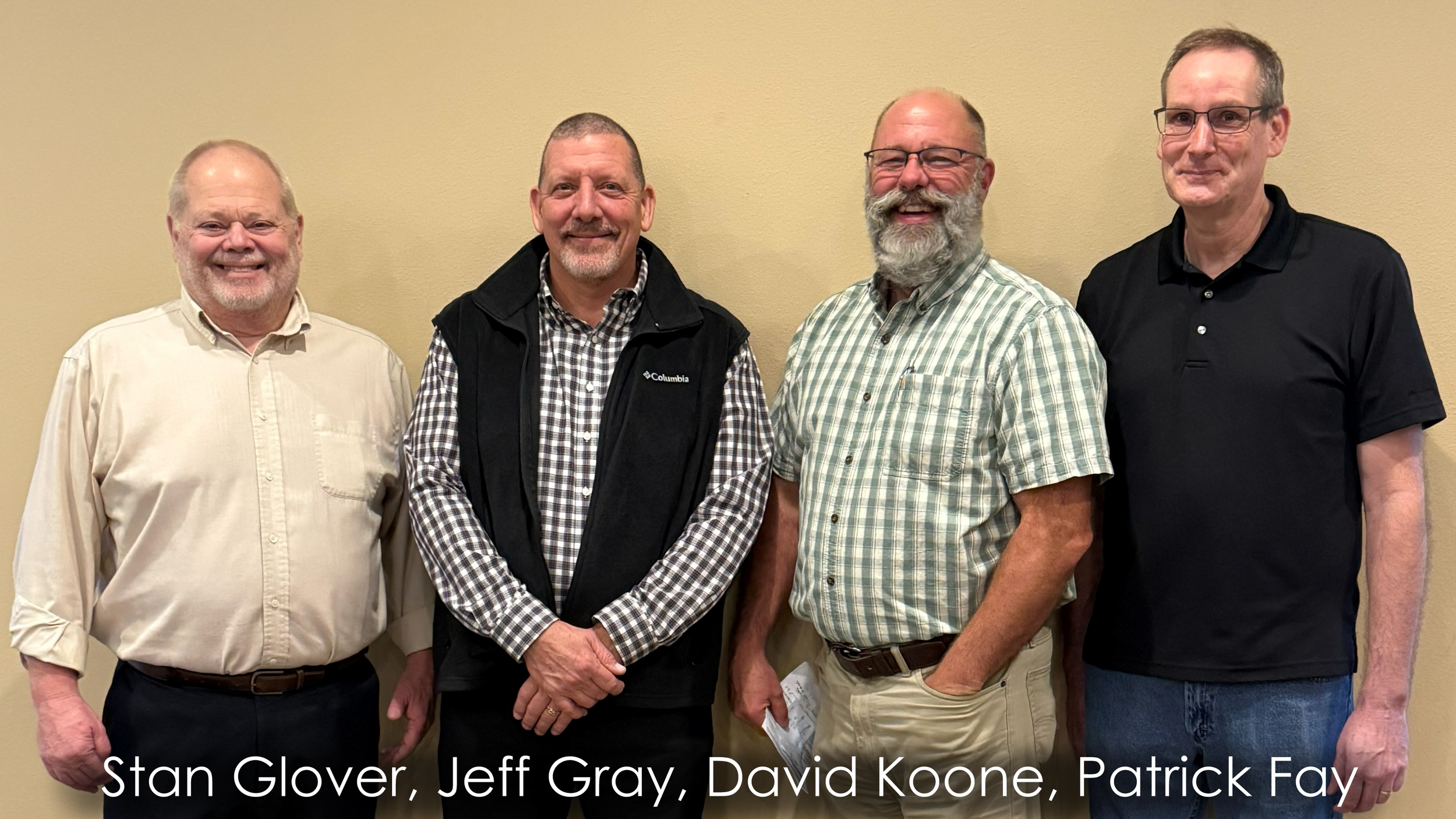 Four men standing side by side in front of a beige wall, smiling. From left to right: Stan Glover, Jeff Gray, David Koone, Patrick Fay.