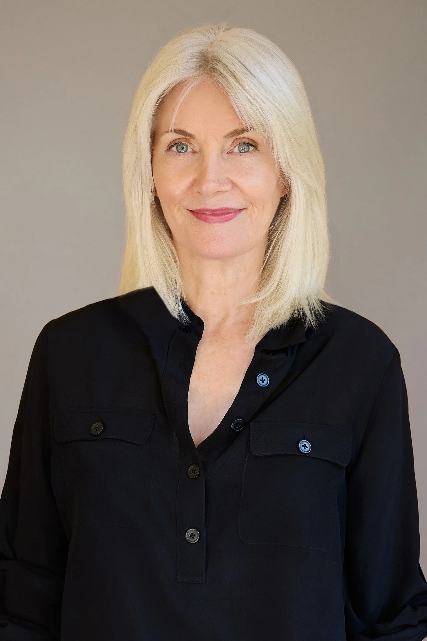 A woman with blonde hair and blue eyes smiling, wearing a black button-up shirt, against a neutral background.