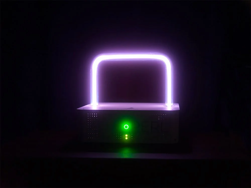 A PERL Rife device surrounded in darkness, with a rectangular violet plasma glowing in the dark above a glowing green indicator.