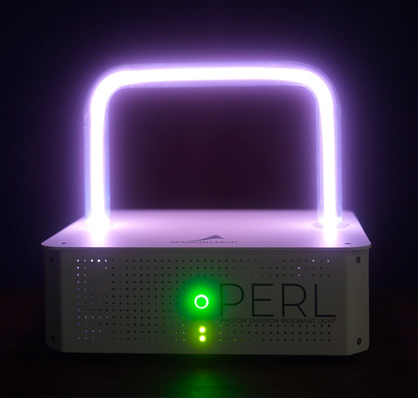 A PERL Rife device surrounded in darkness, with a rectangular violet plasma glowing in the dark above a glowing green indicator. The image of the device is more clear than the other two images and the letters PERL are clearly seen.
