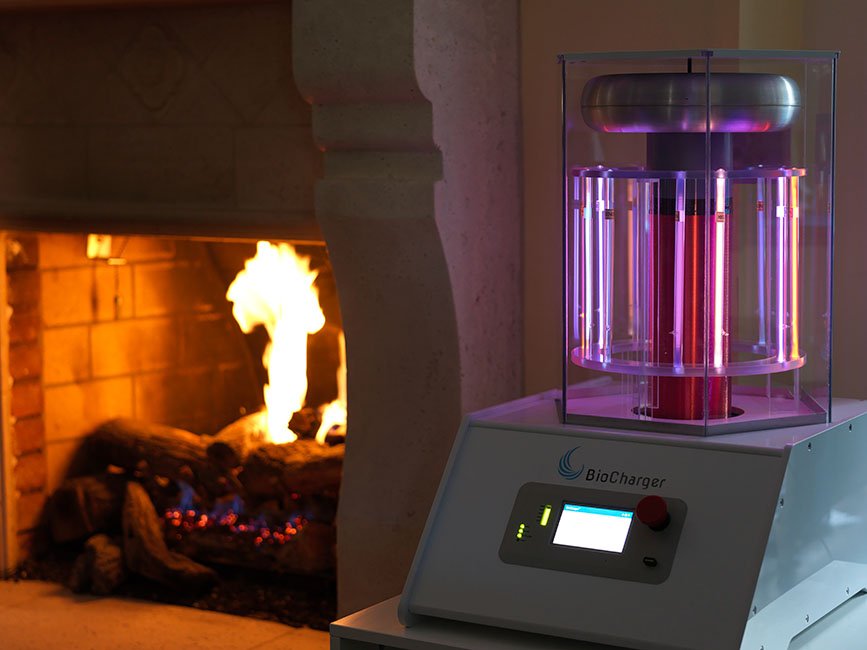 A scientific machine labeled 'BioCharger' with a glowing purple and pink light, placed next to a lit and erupting fireplace.