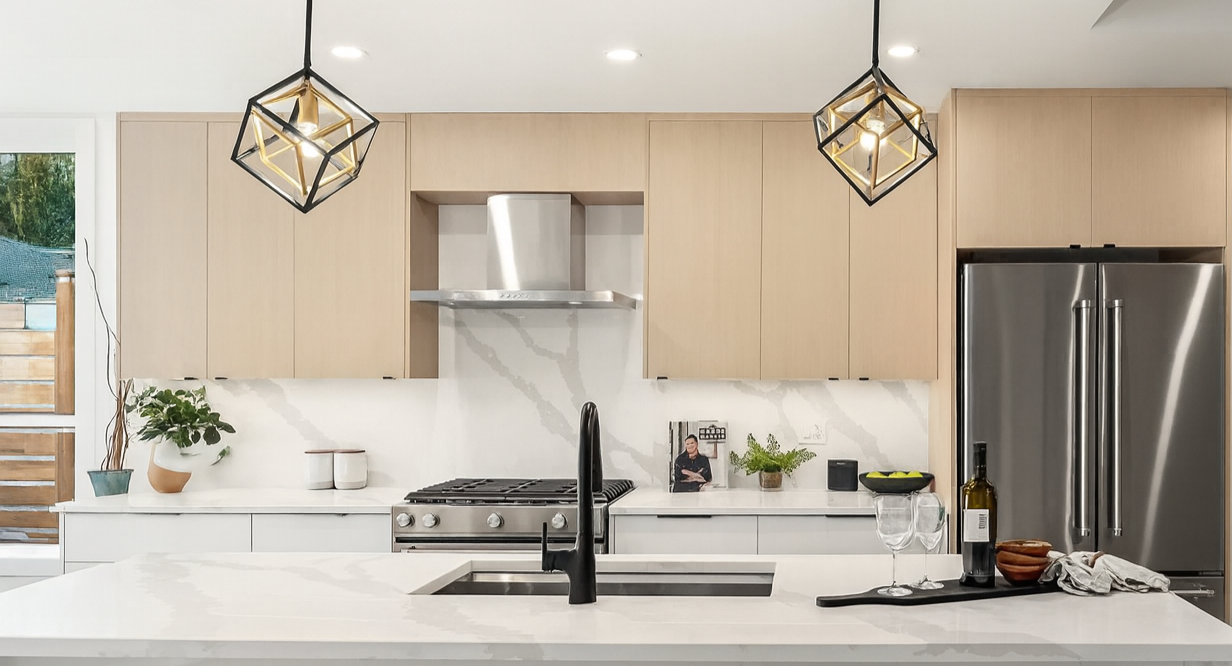 Modern kitchen with a white island, beige upper cabinets, stainless steel appliances, black geometric pendant lights, and various decorative items.