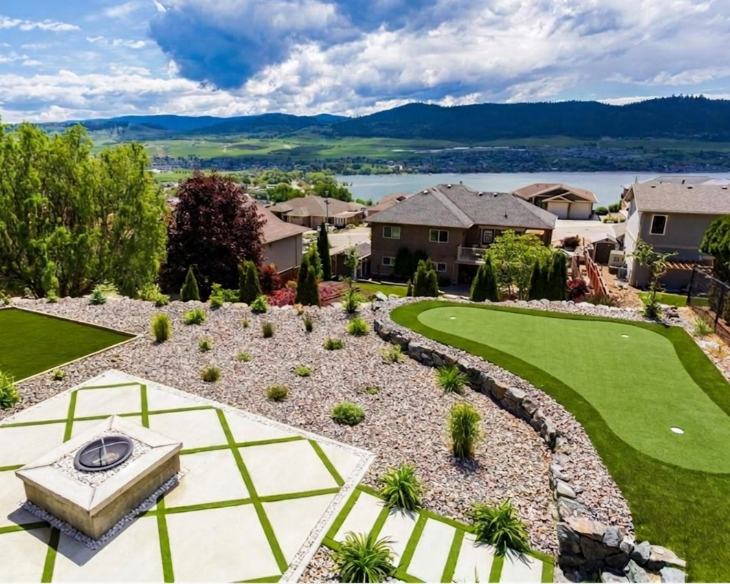 A backyard landscape with a pond, hillside houses, and a lake with mountains in the background, under a cloudy sky.