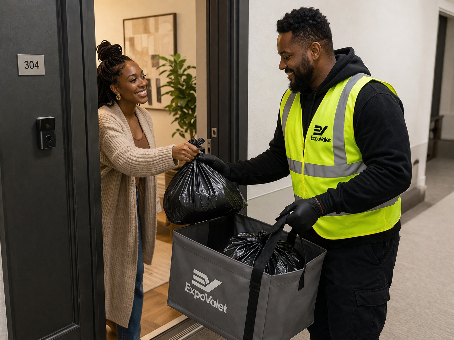 A delivery person wearing a high-visibility vest handing a black plastic bag to a woman at her apartment door.