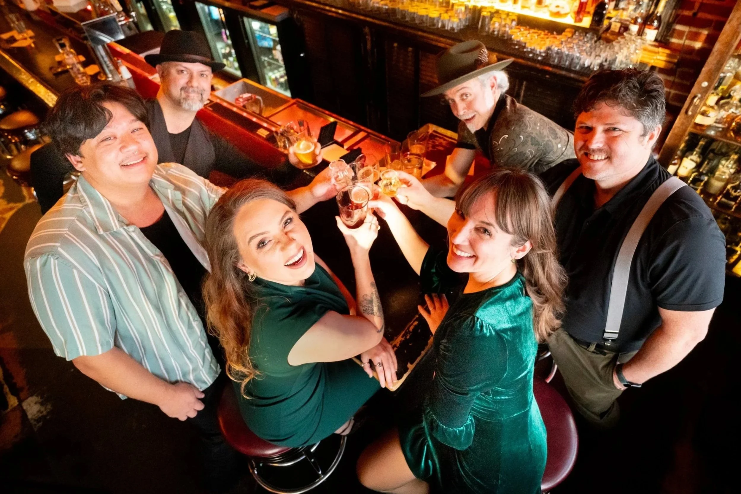 Group of friends at a bar celebrating with drinks, seen from above, smiling and toasting.