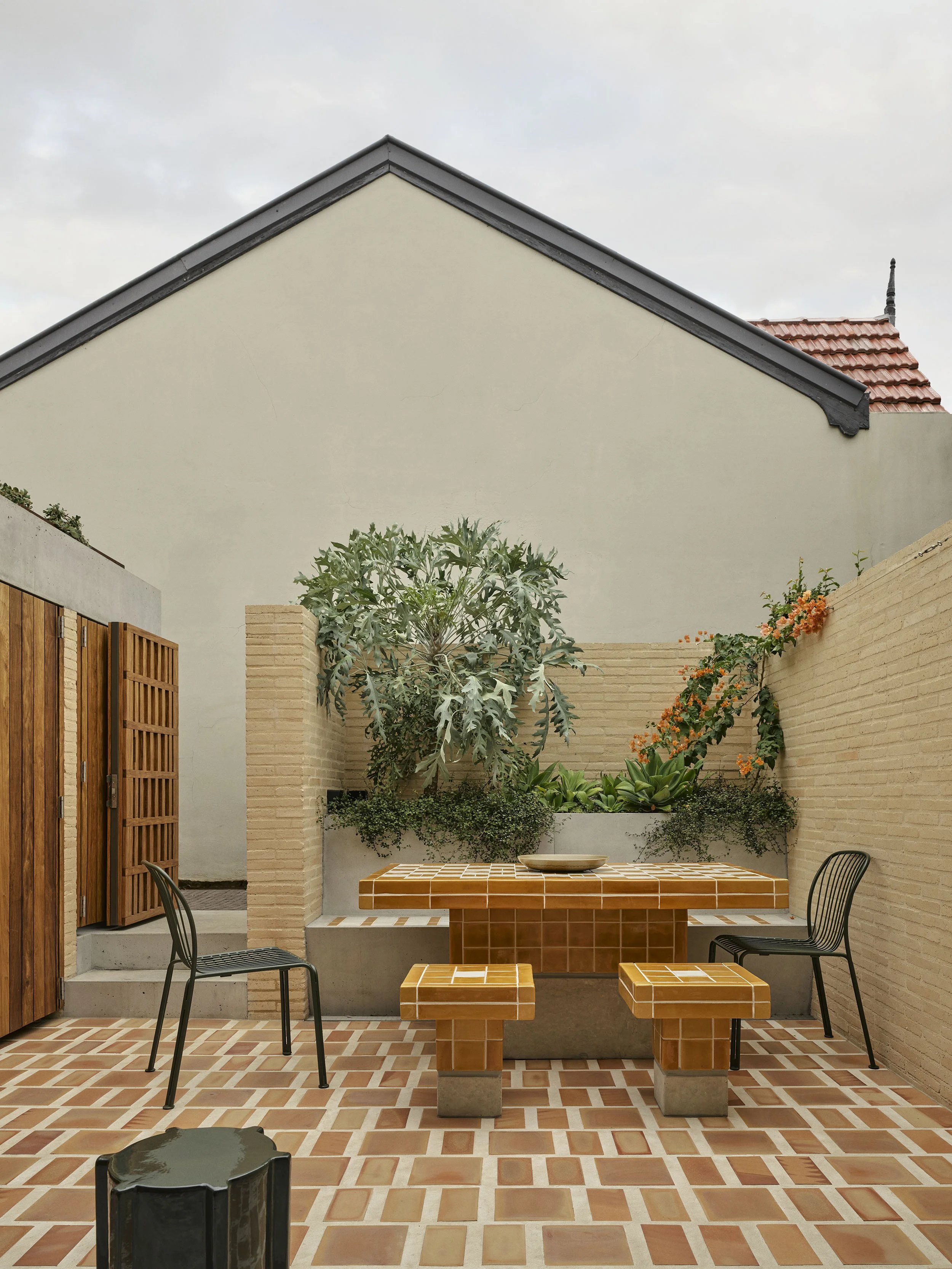 Tiled outdoor table and tiled outdoor stools and built-in concrete seat with terracotta tiles with maxi-grout in Sydney terrace renovation by heritage architects Sydney Muci.