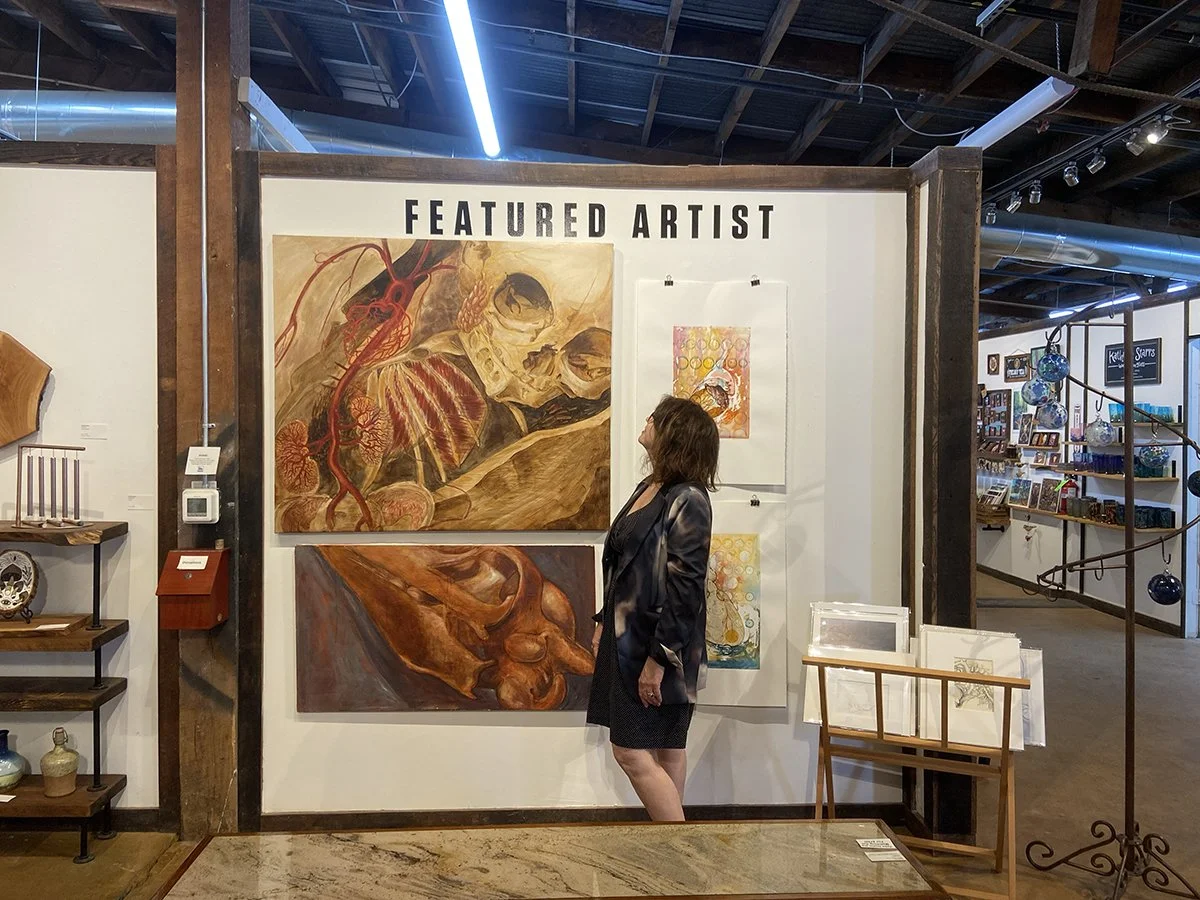 Picture of the artist in front of several pieces in a gallery space