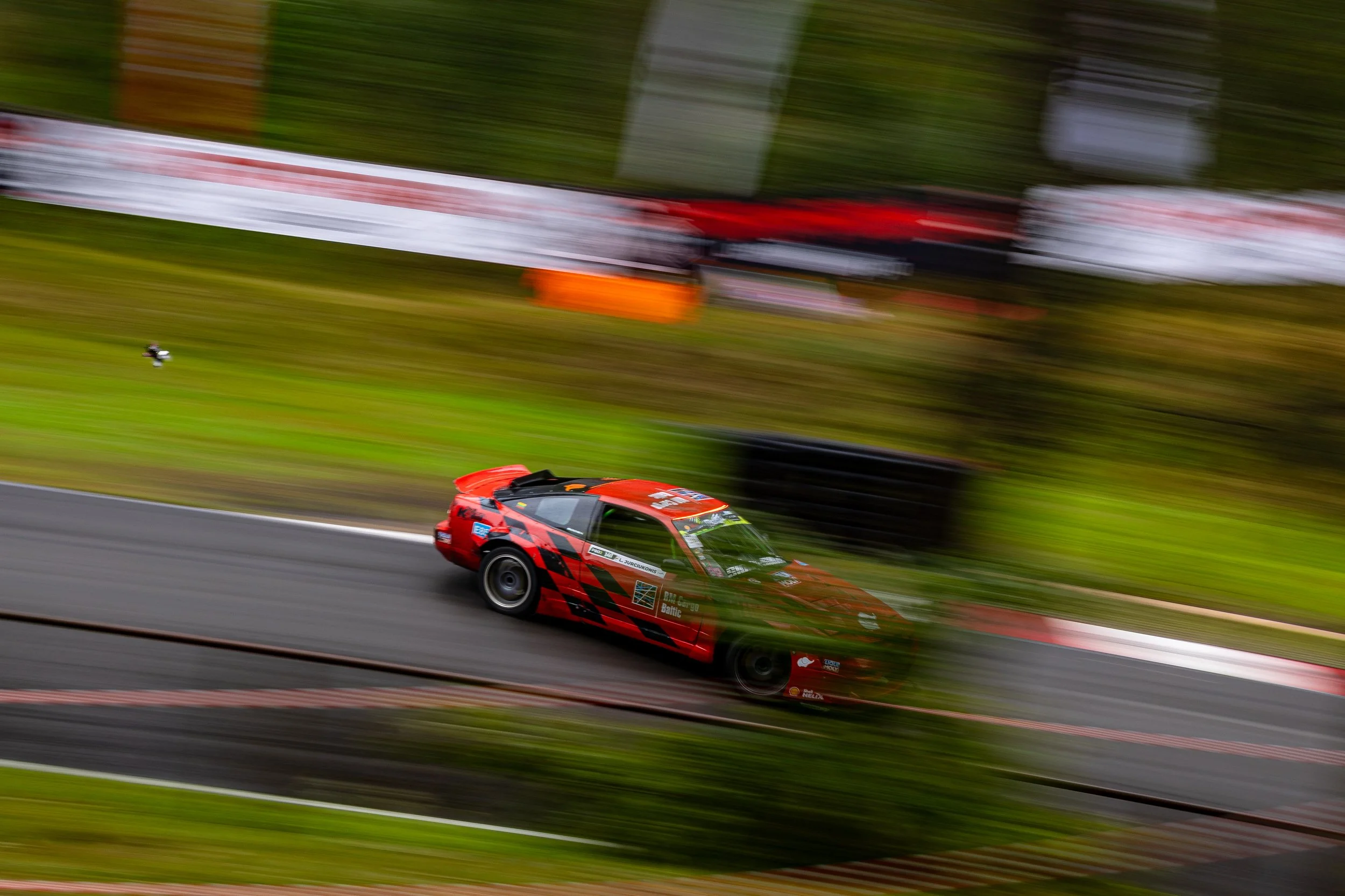 A red race car speeding on a race track with blurred surroundings and tire barriers in the background, captured with motion blur.