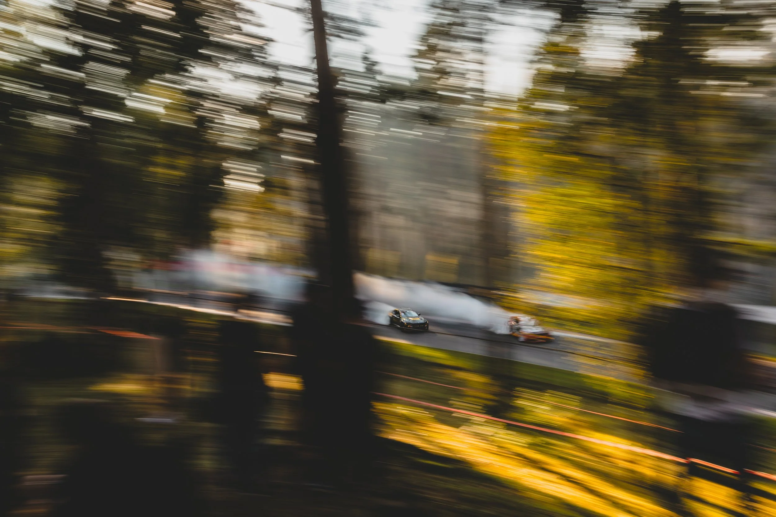 A blurred photo of a car crash scene on a street with trees and smoke.
