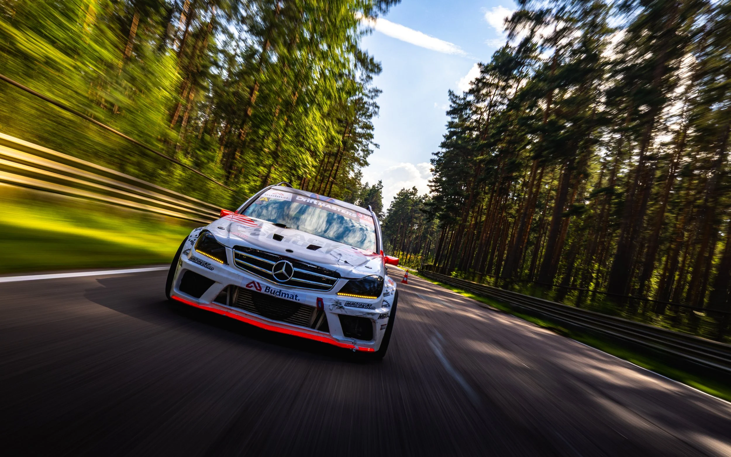A white race car with Mercedes-Benz logo accelerating on a forested race track during the day.