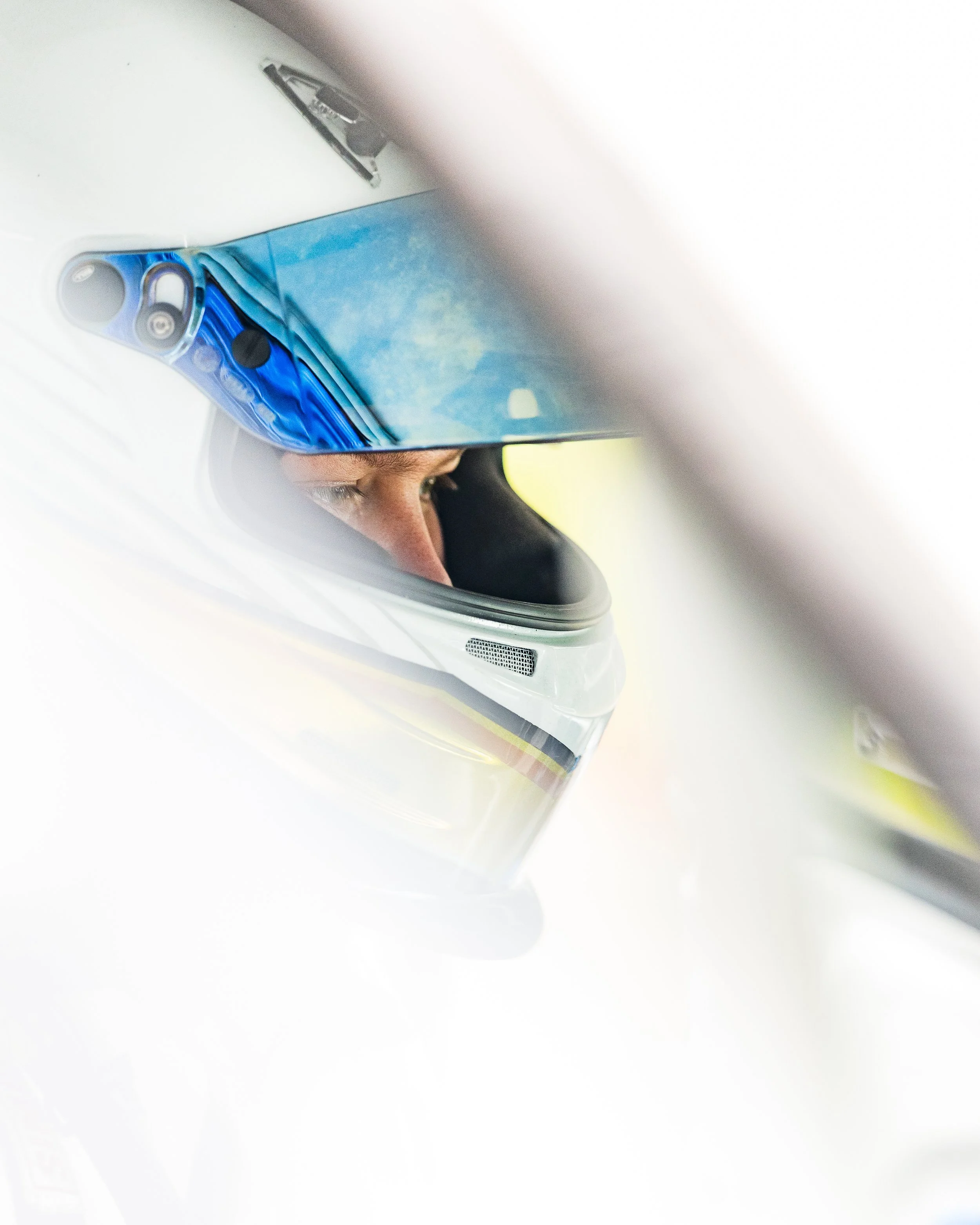 Close-up of a person wearing a racing helmet with a reflective visor, with only part of their face visible.