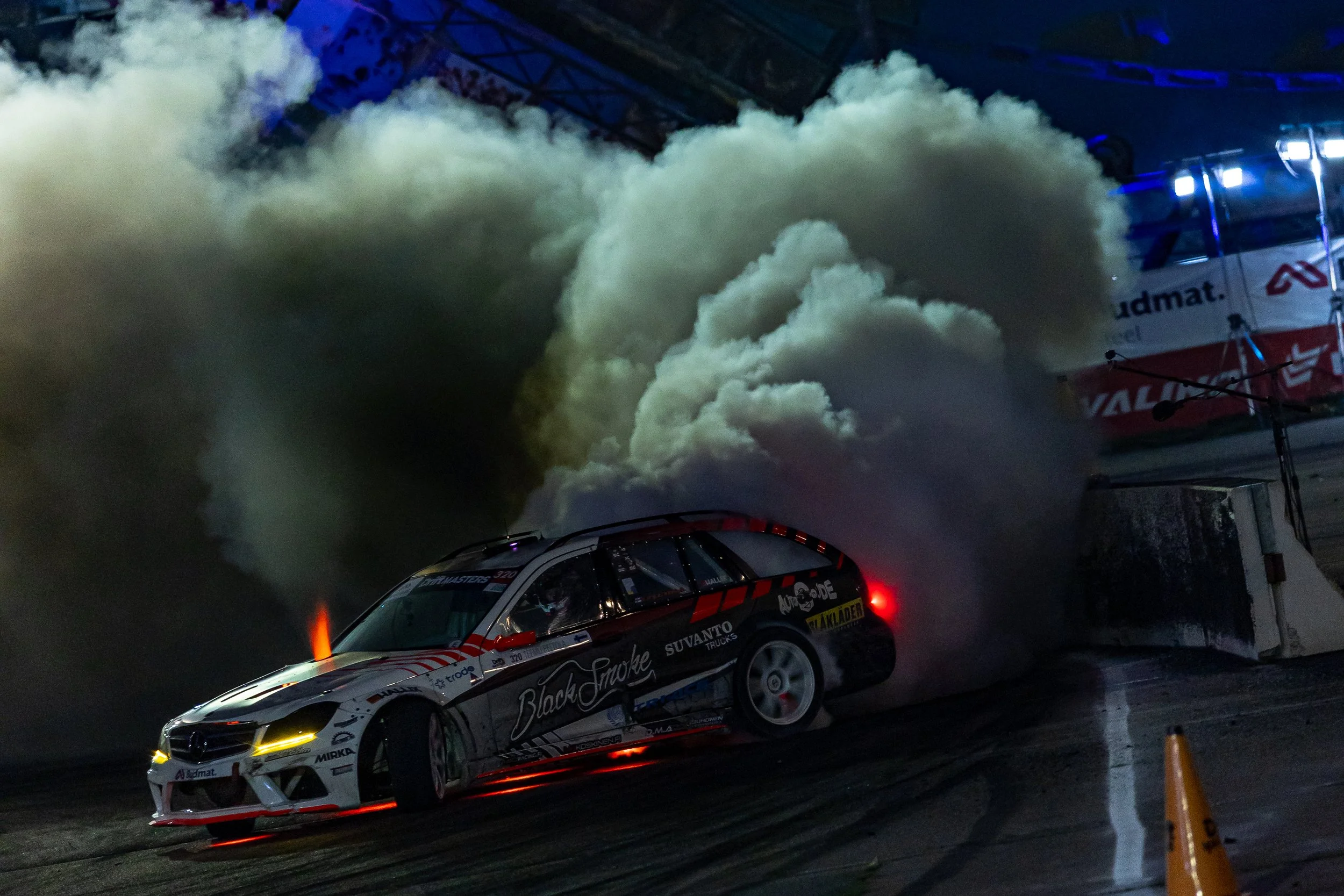 Race car on a track emitting smoke during a nighttime racing event.